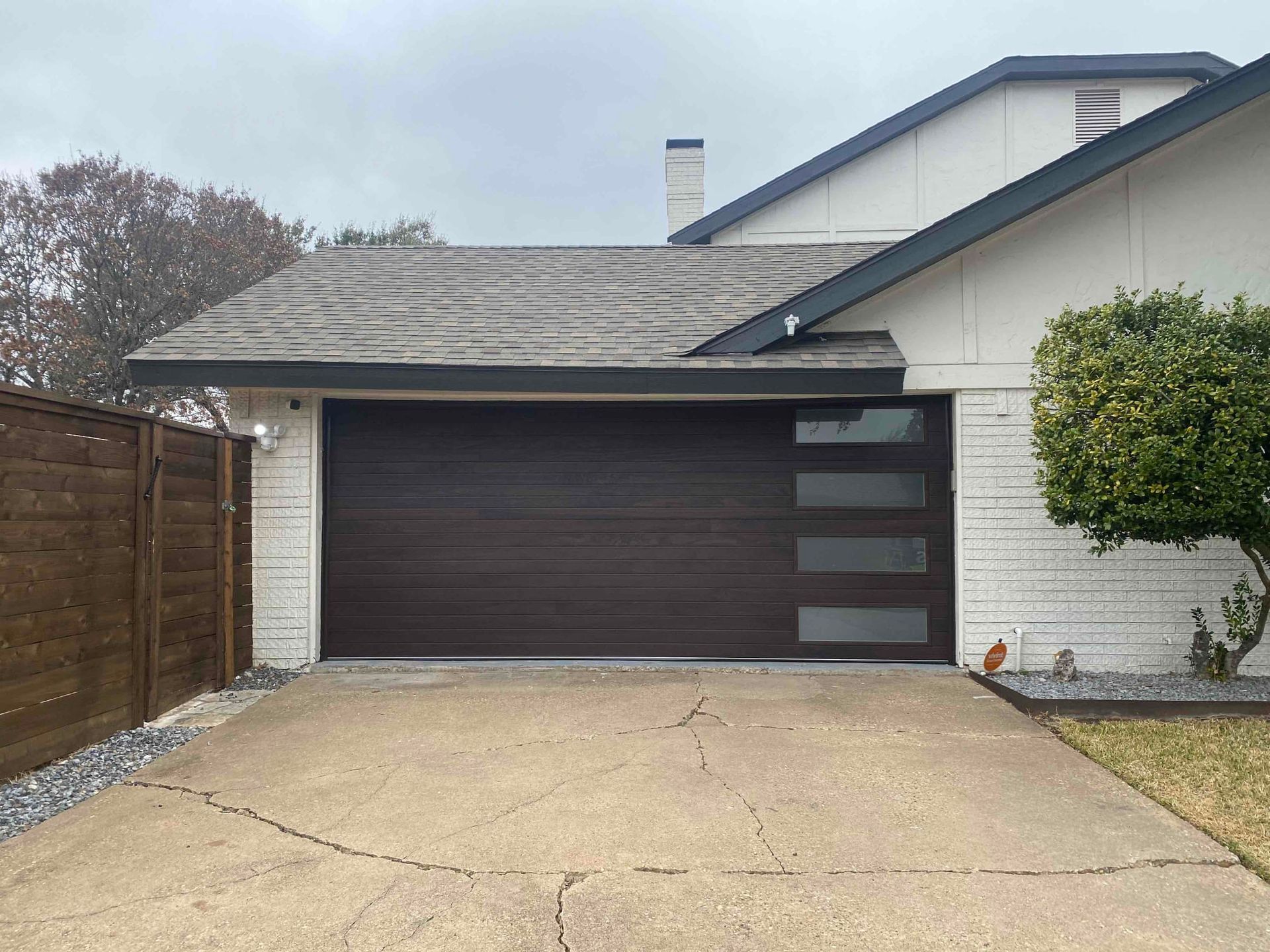 A driveway leading to a modern house with a dark brown horizontal-plank garage door featuring a vertical row of windows.