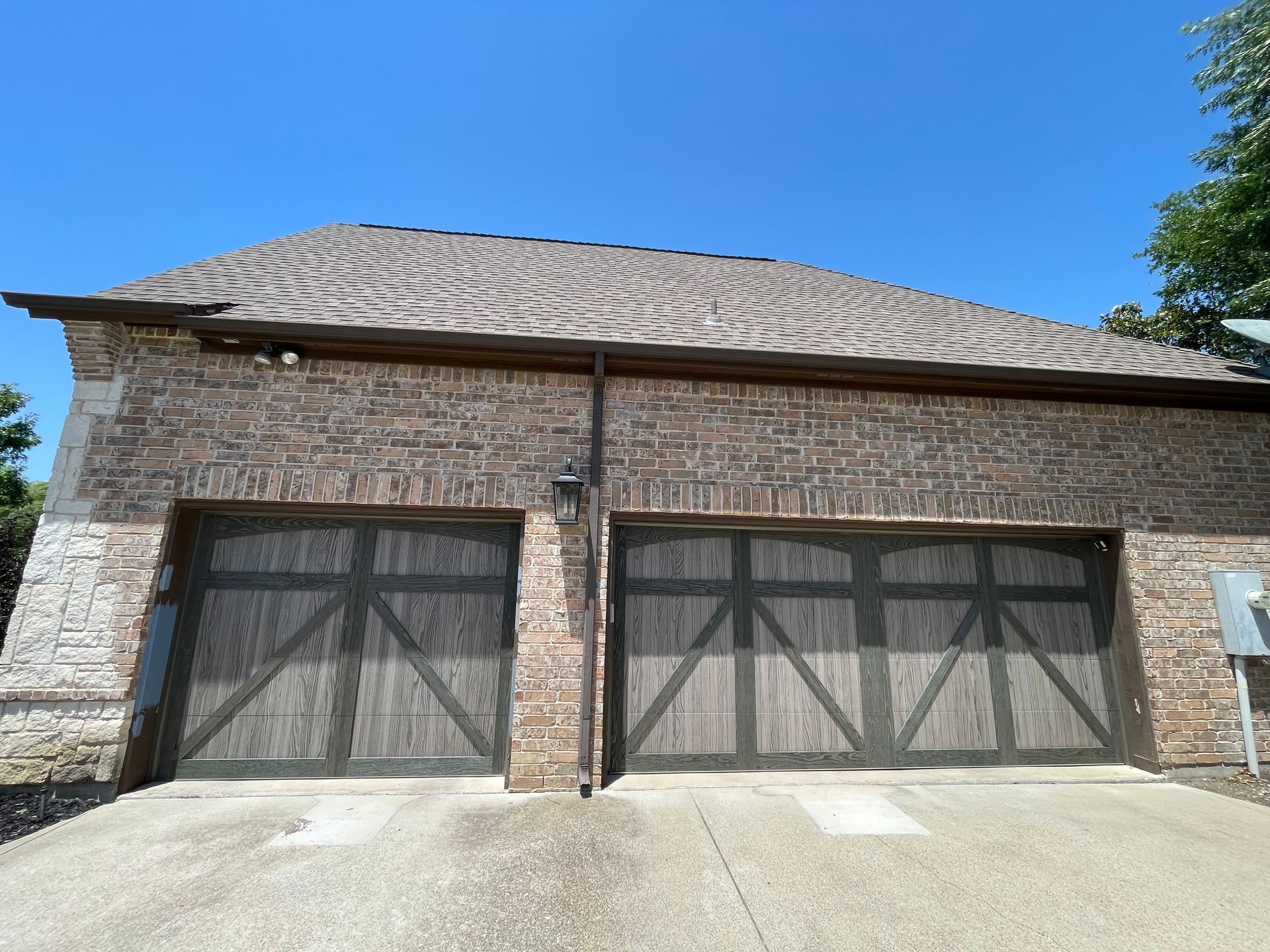A detached, two-car brick garage with a shingled roof, dark wood-look carriage-style doors, and a concrete driveway.