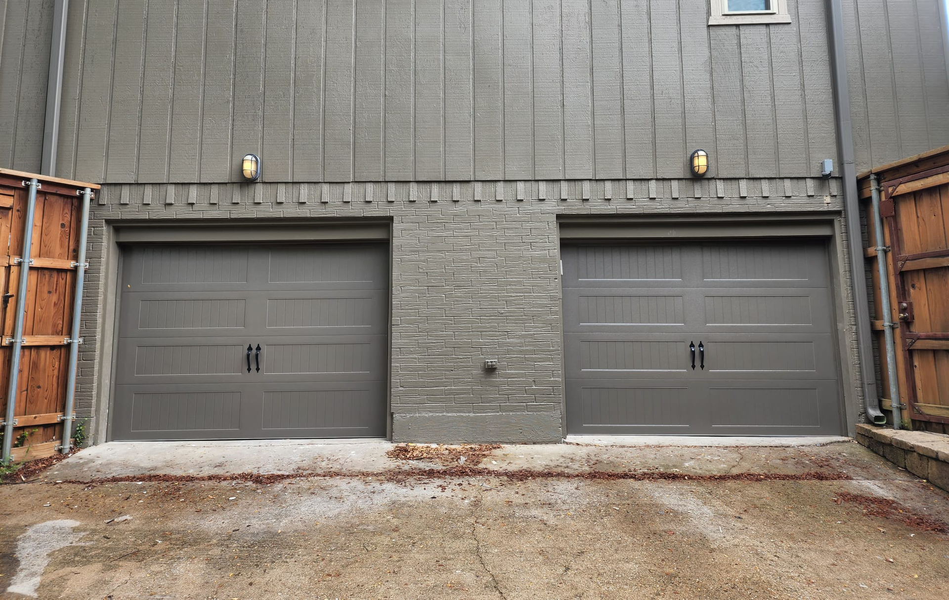 Two gray garage doors under a gray building. Decorative brick separates them.