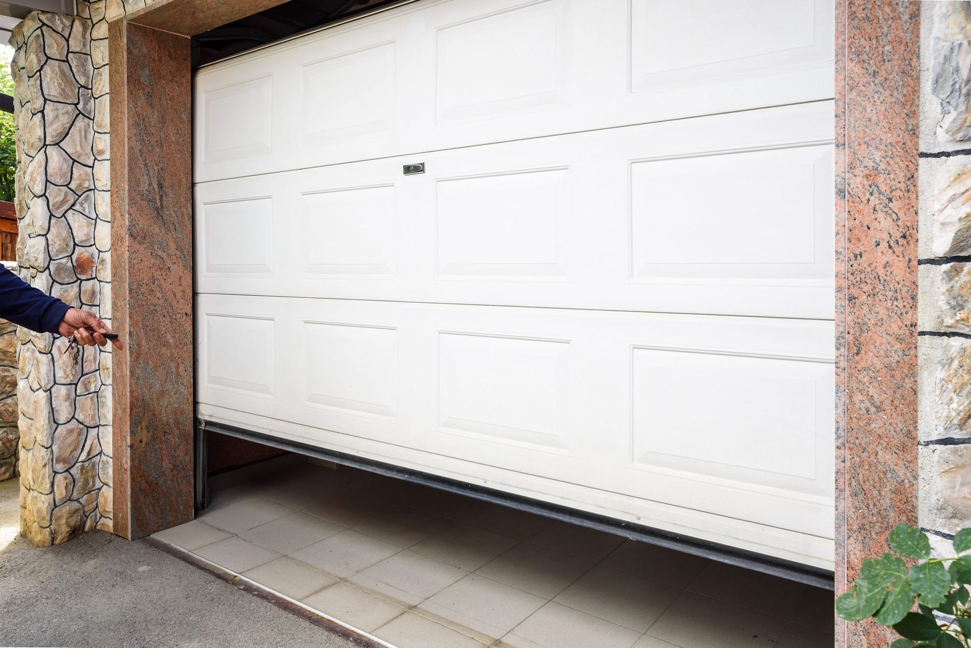 Garage door opening, operated by a person holding a remote. White door, stone facade.
