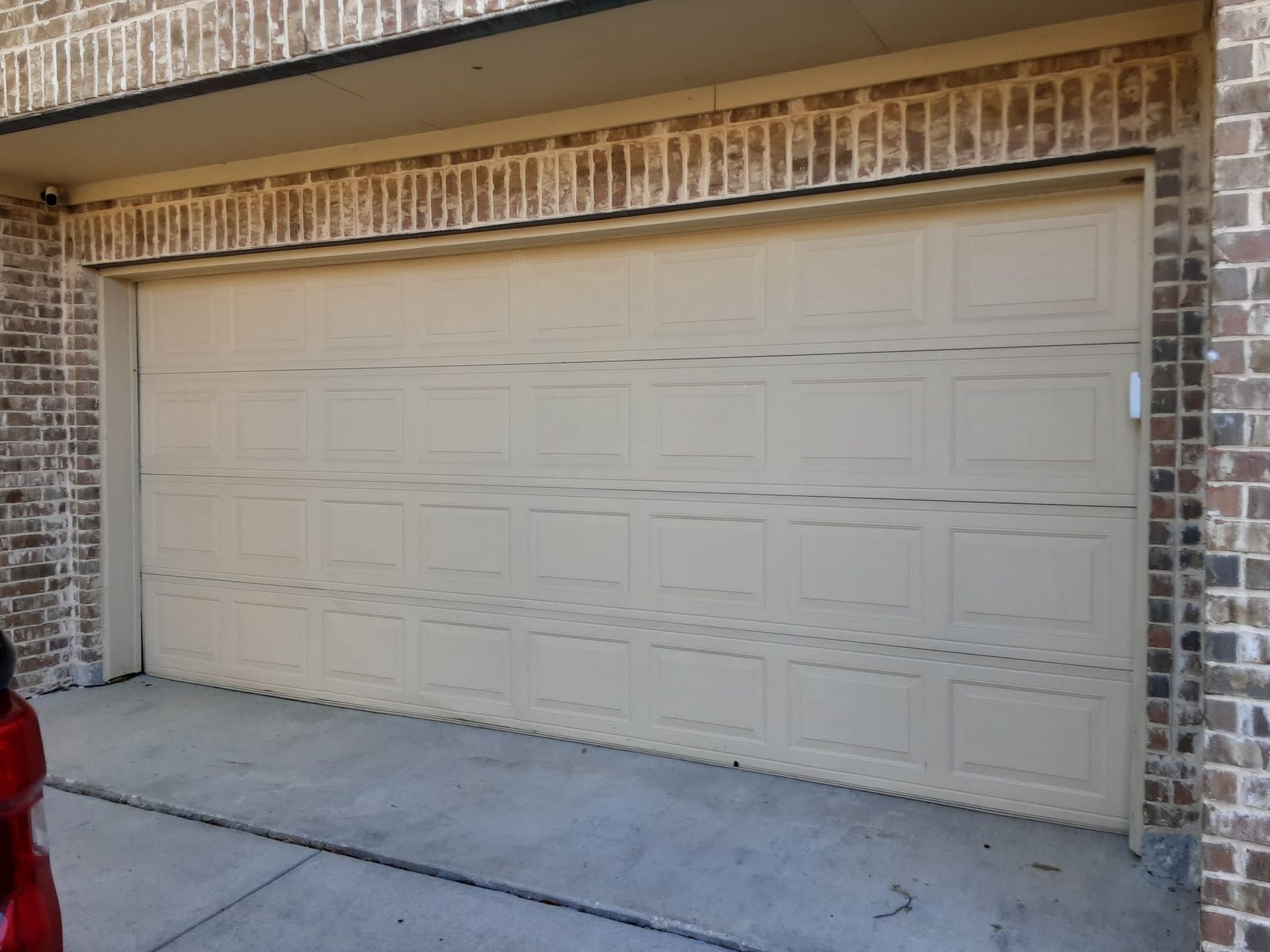 Beige garage door on a brick house; concrete driveway.