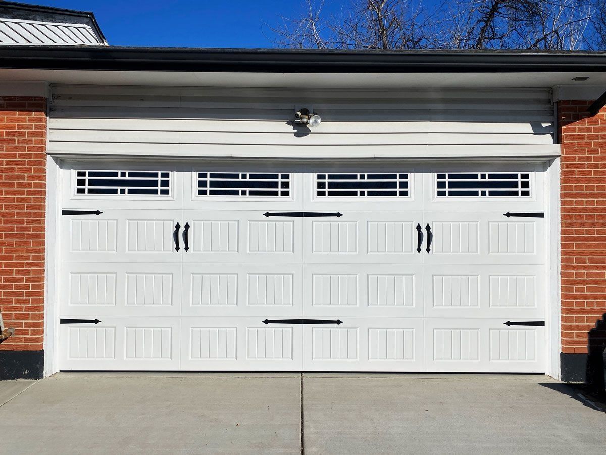 White garage door with black hardware, set in a brick and concrete building.