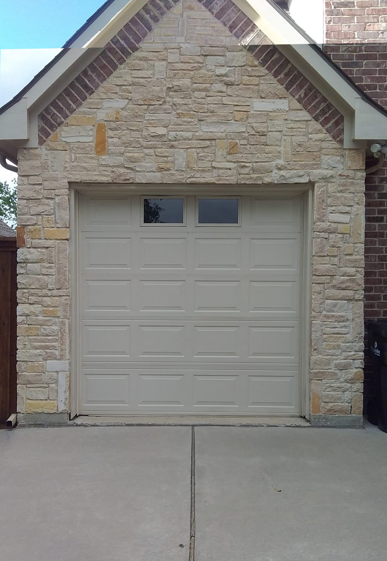 Tan garage door with two small windows, set in a stone wall.