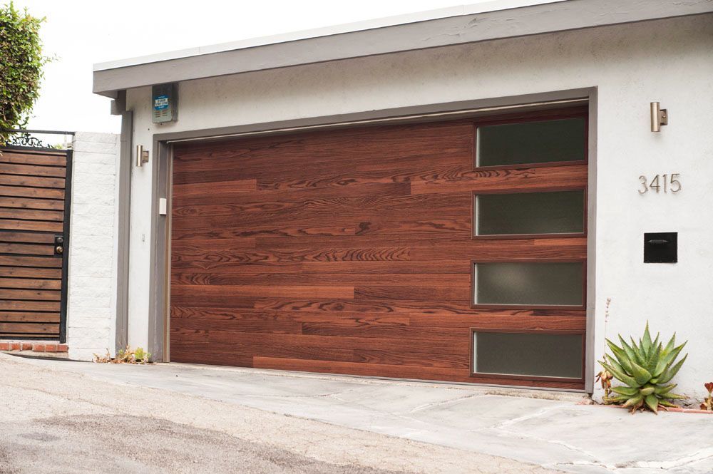 A modern garage door featuring horizontal wood paneling and a vertical row of four frosted glass windows on the right.