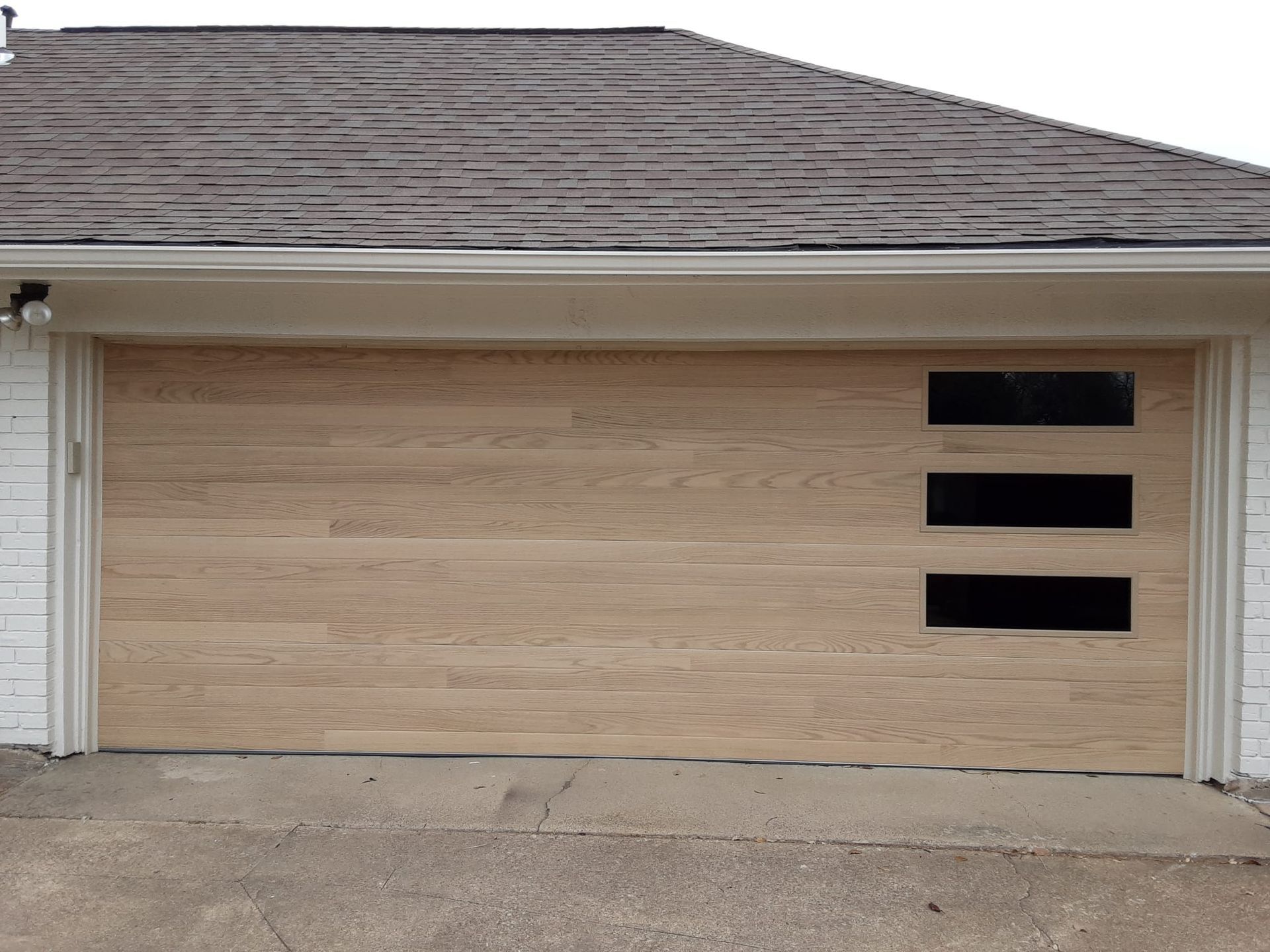 A light wood-toned garage door with three stacked horizontal rectangular windows on the right side.