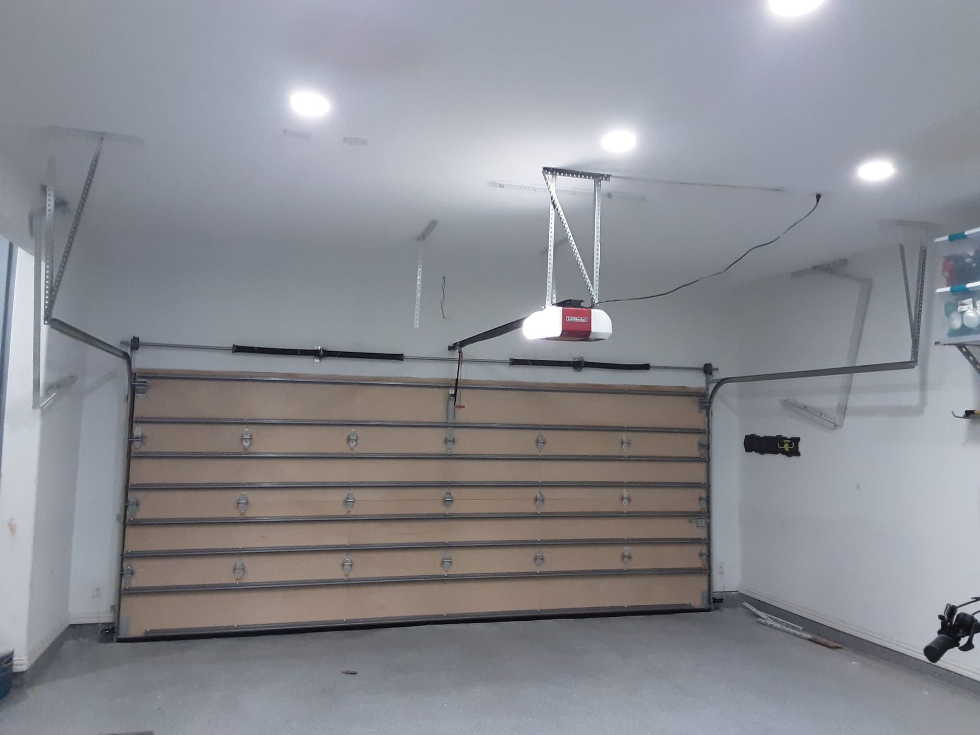 A tan garage door is installed in a room with white walls, recessed ceiling lights, and a motor-driven opener mechanism.