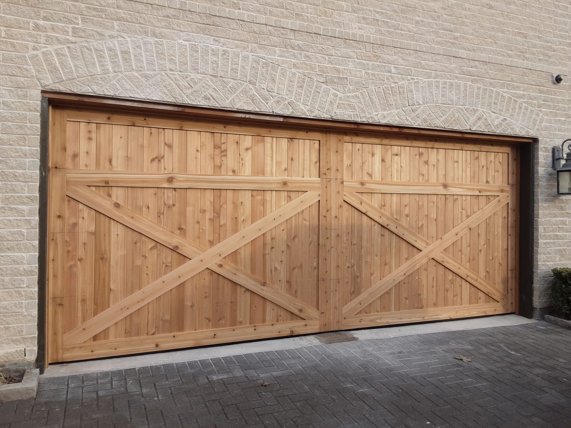 A double-wide wooden garage door with an X-shaped cross-brace design on a light-colored brick building.