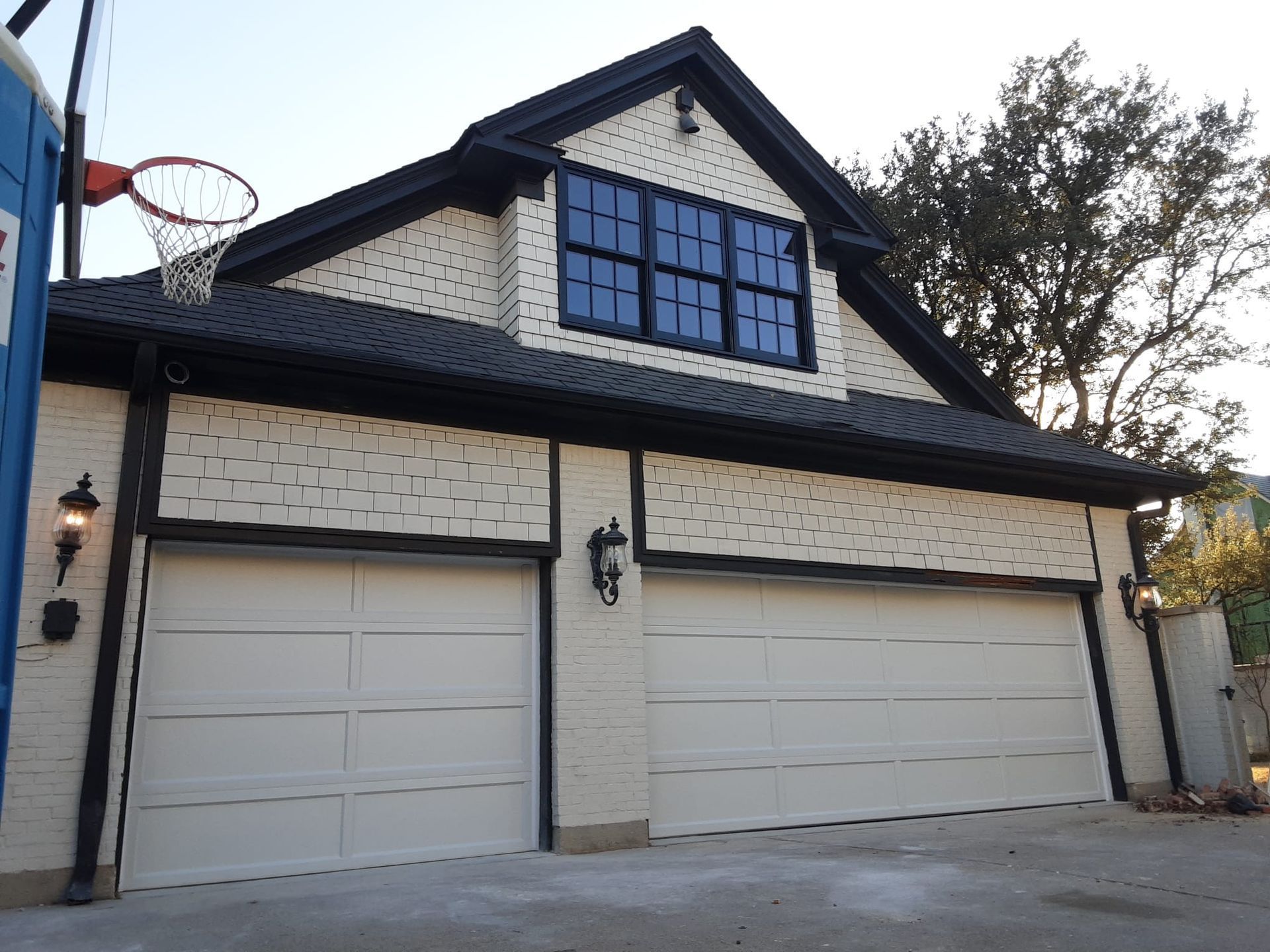 A two-car garage with white brick walls, black trim, and a small attic window under a gabled roof.