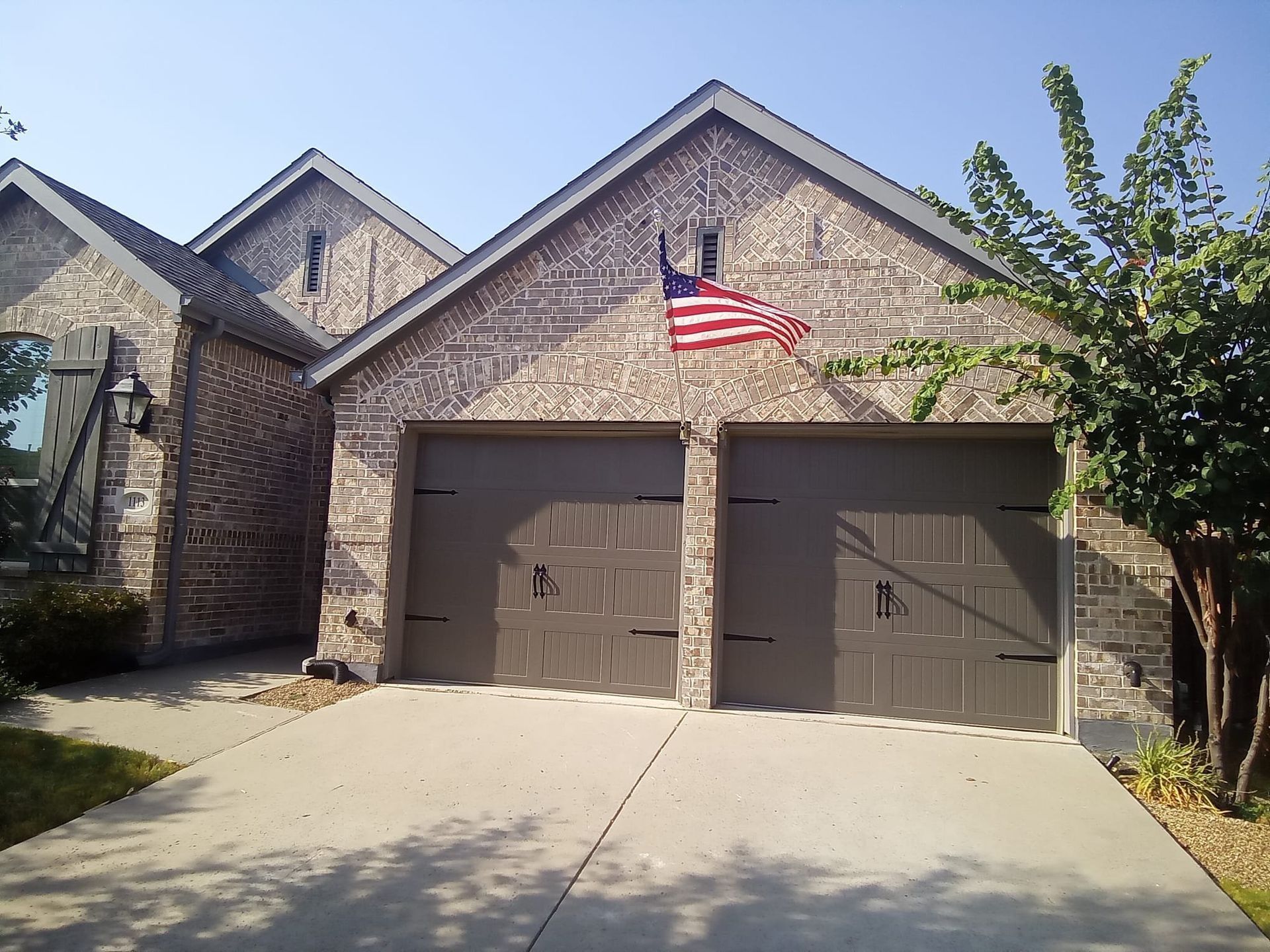 A brick house with a two-car garage and a small American flag hanging above the doors.
