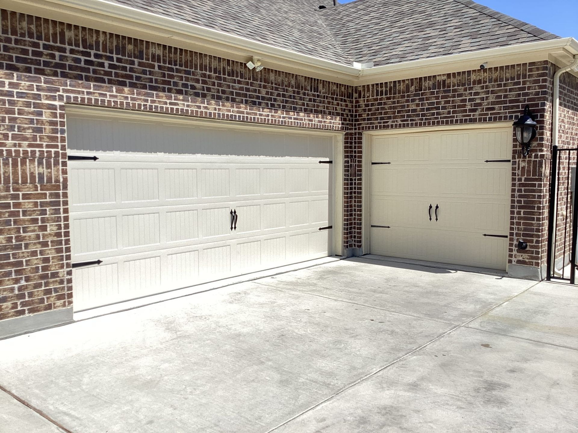 Two beige, raised-panel garage doors set into a brick exterior wall, facing a concrete driveway.
