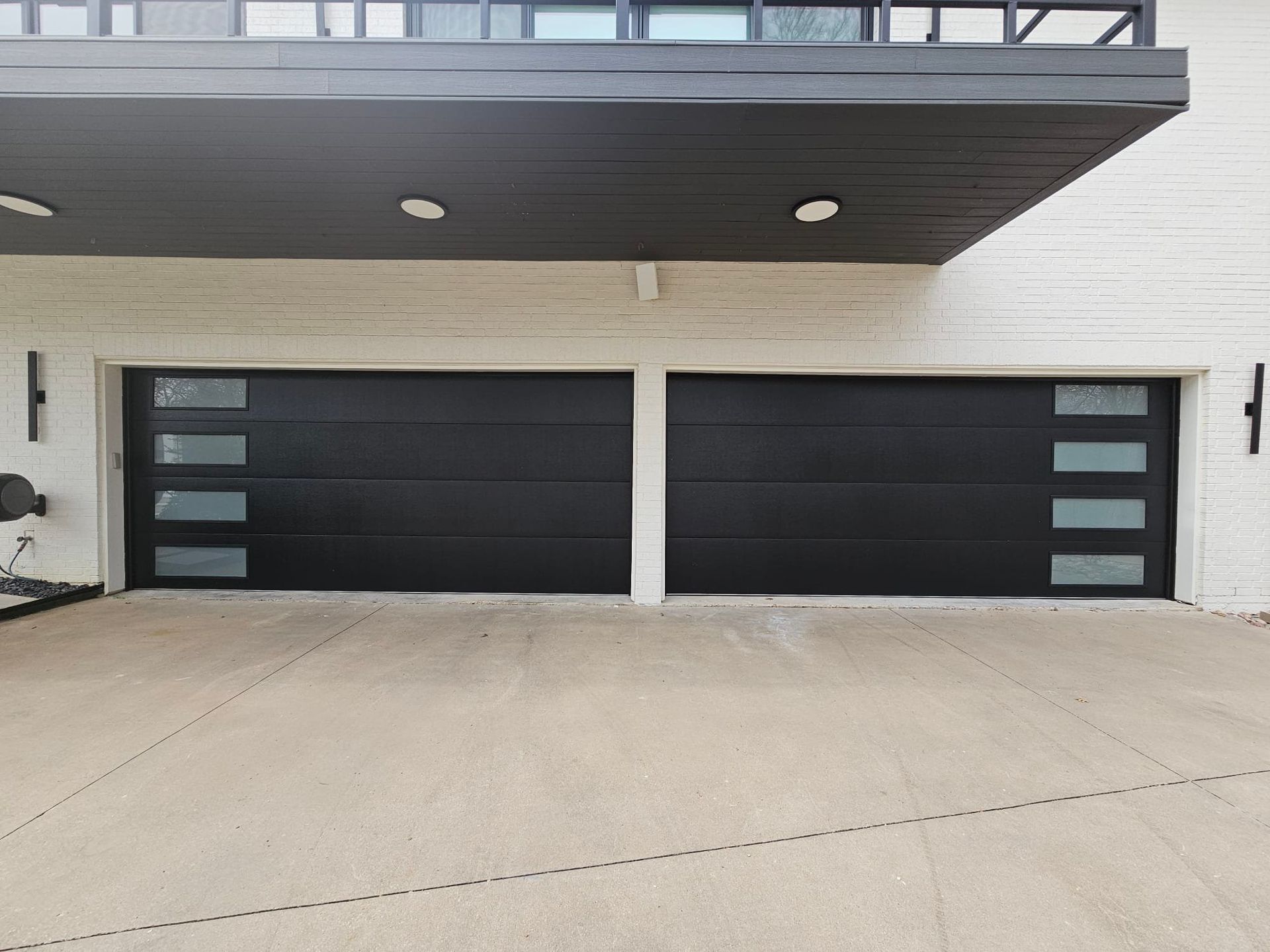 Two black, horizontal-paneled garage doors with four stacked, frosted-glass rectangular windows on the outer sides.