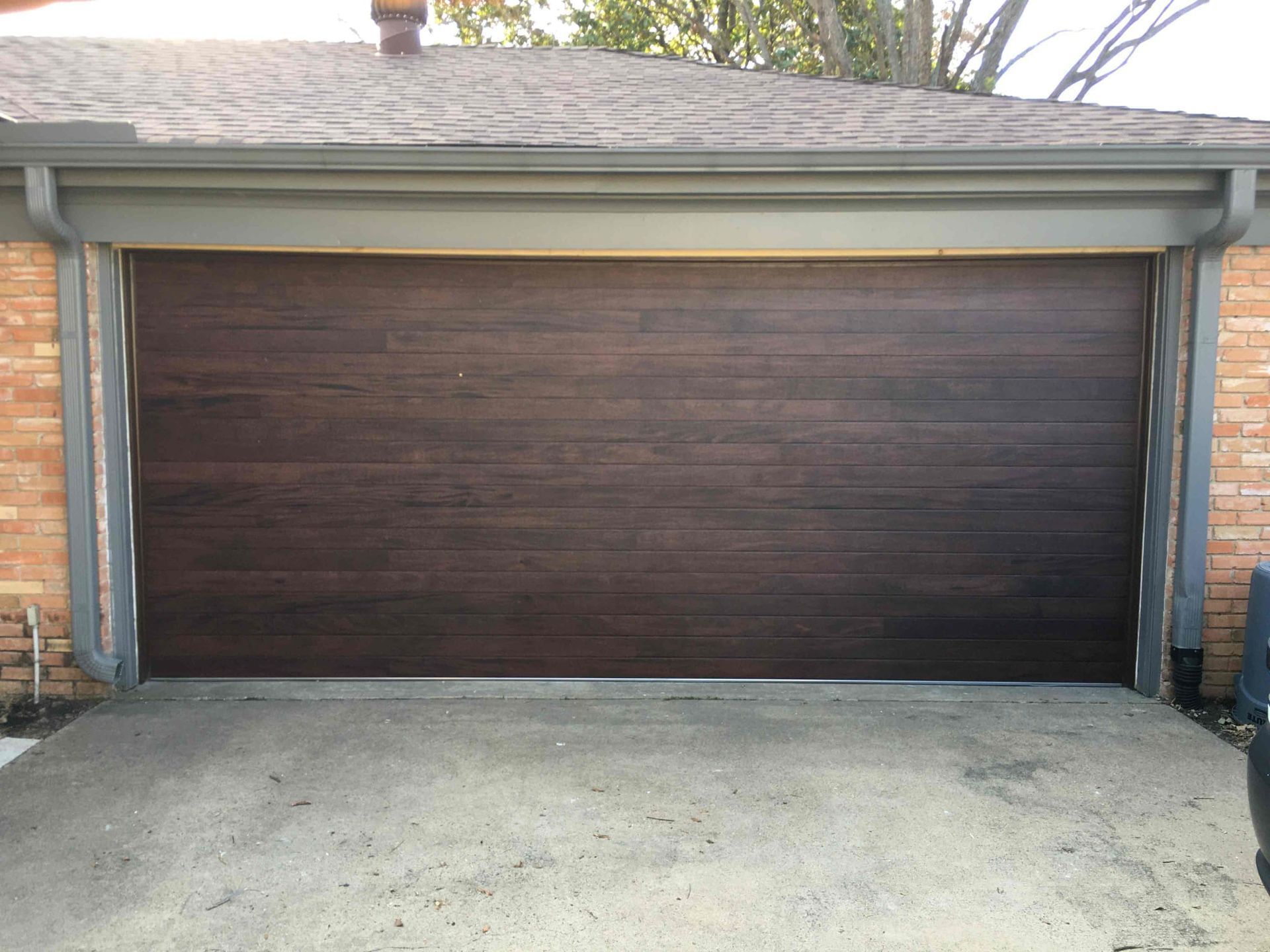 A dark, wood-grain texture garage door set in a brick exterior wall with grey trim.