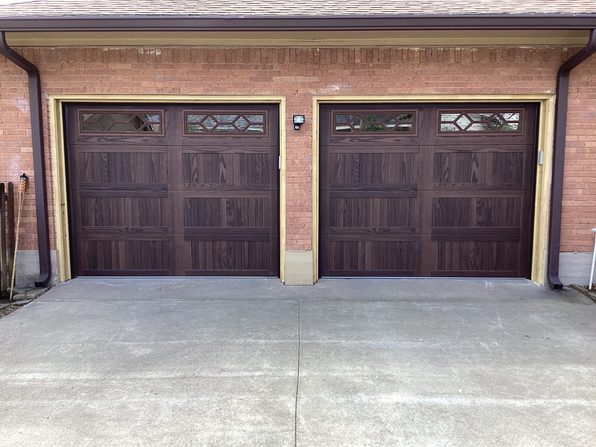 Two dark brown wooden double garage doors with small decorative windows, set in a light brown brick building.