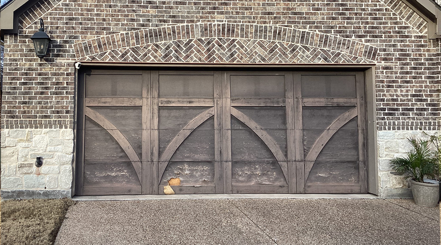Brown brick facade with arched garage door, gravel driveway.