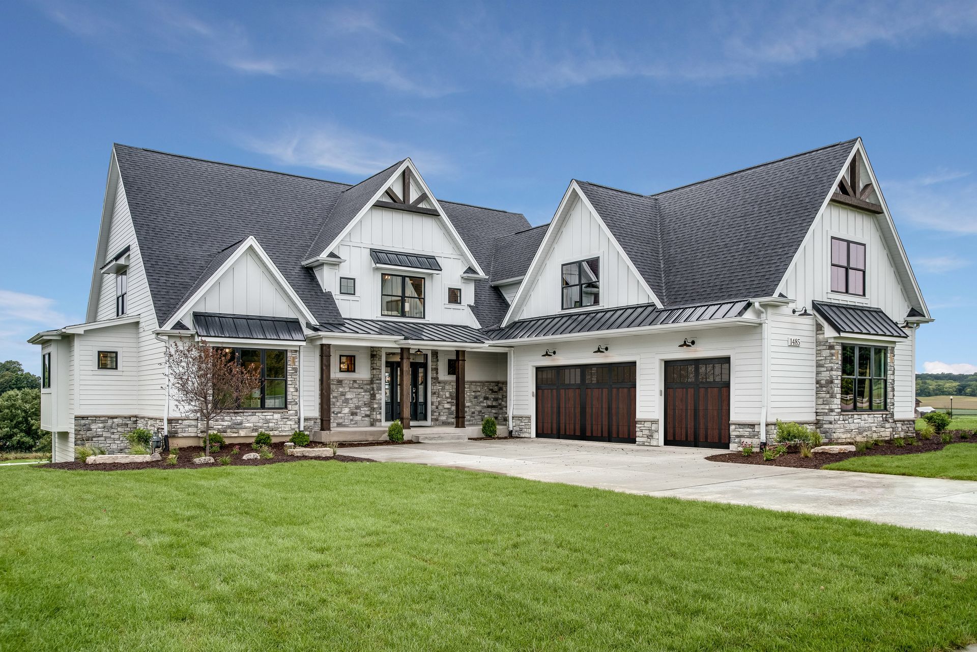 A two-story farmhouse with white siding, dark gabled roofs, stone accents, and a front-facing attached three-car garage.