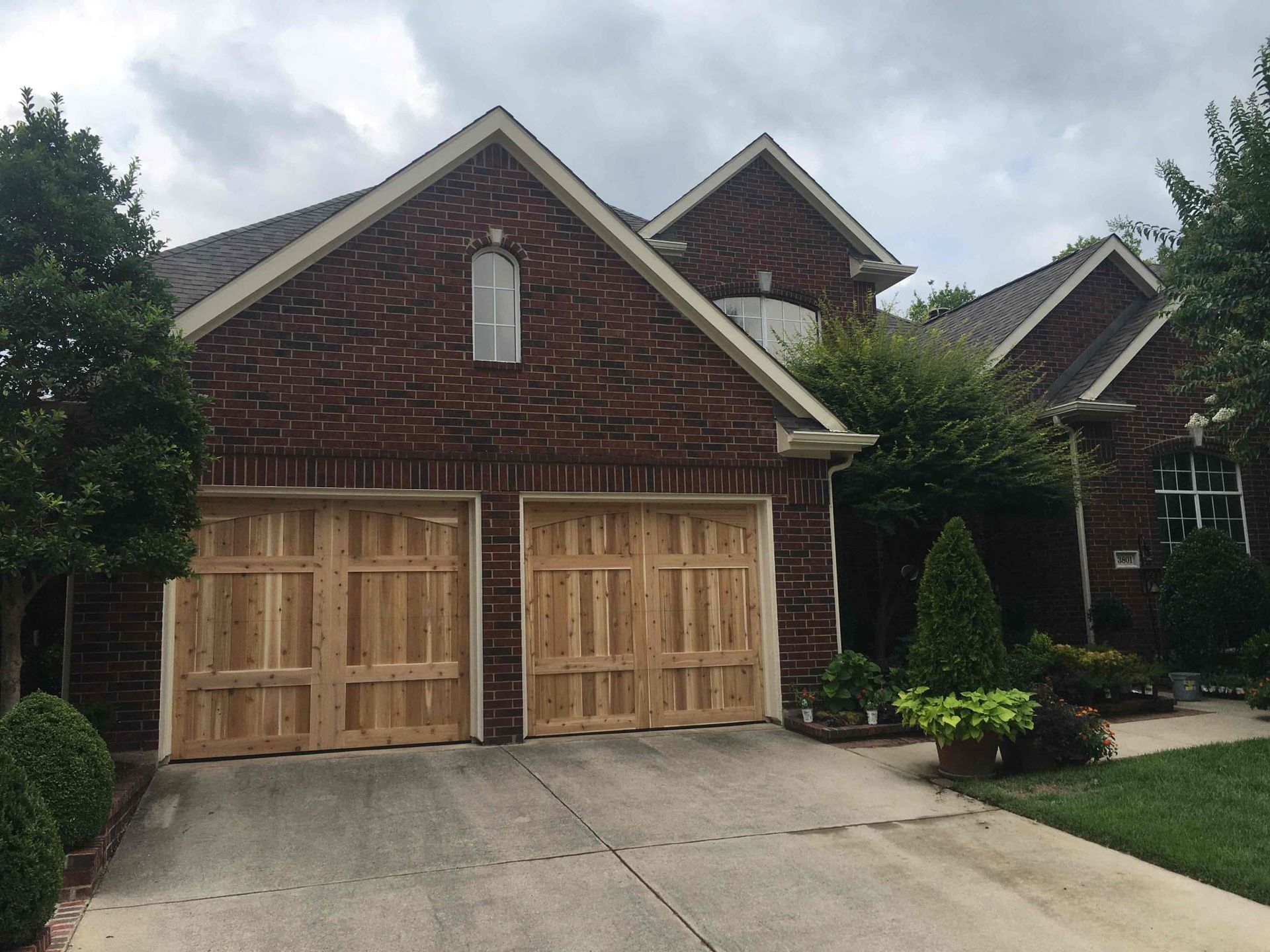 A brick house with two wooden garage doors and a concrete driveway under a cloudy sky.