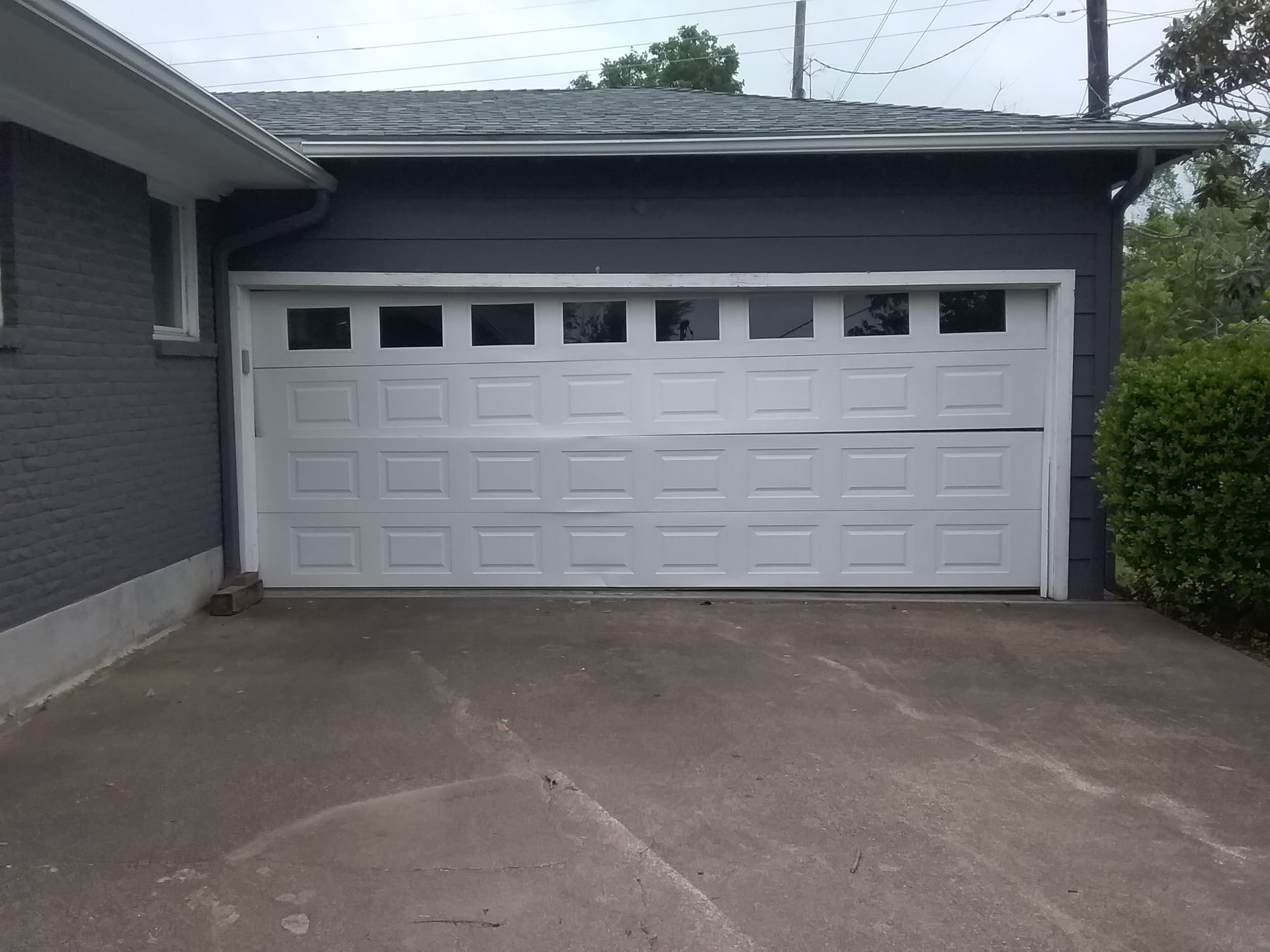 White garage door, partially open, on a gray building with a concrete driveway.