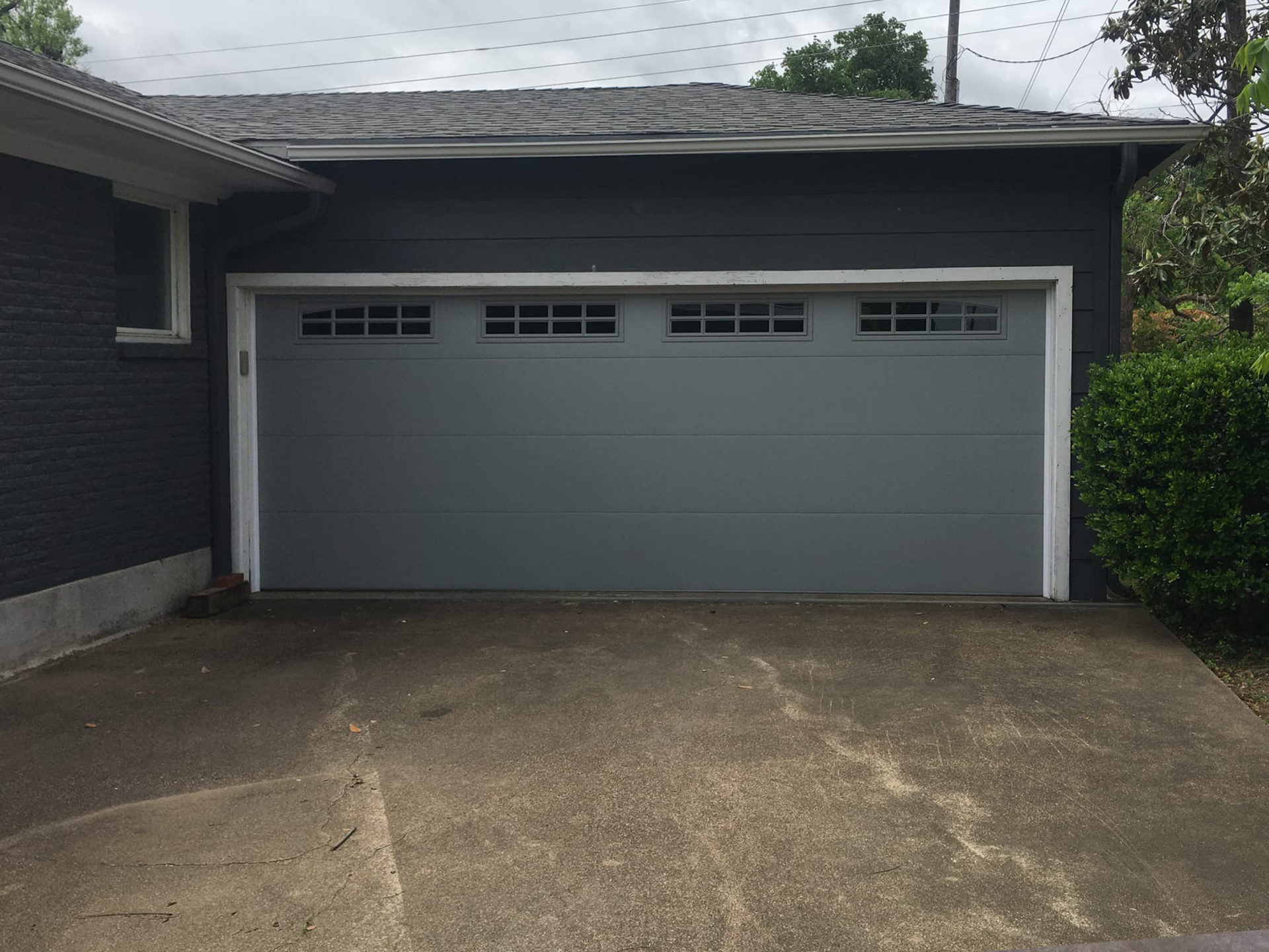 Gray garage door on a gray house, with a concrete driveway in front.