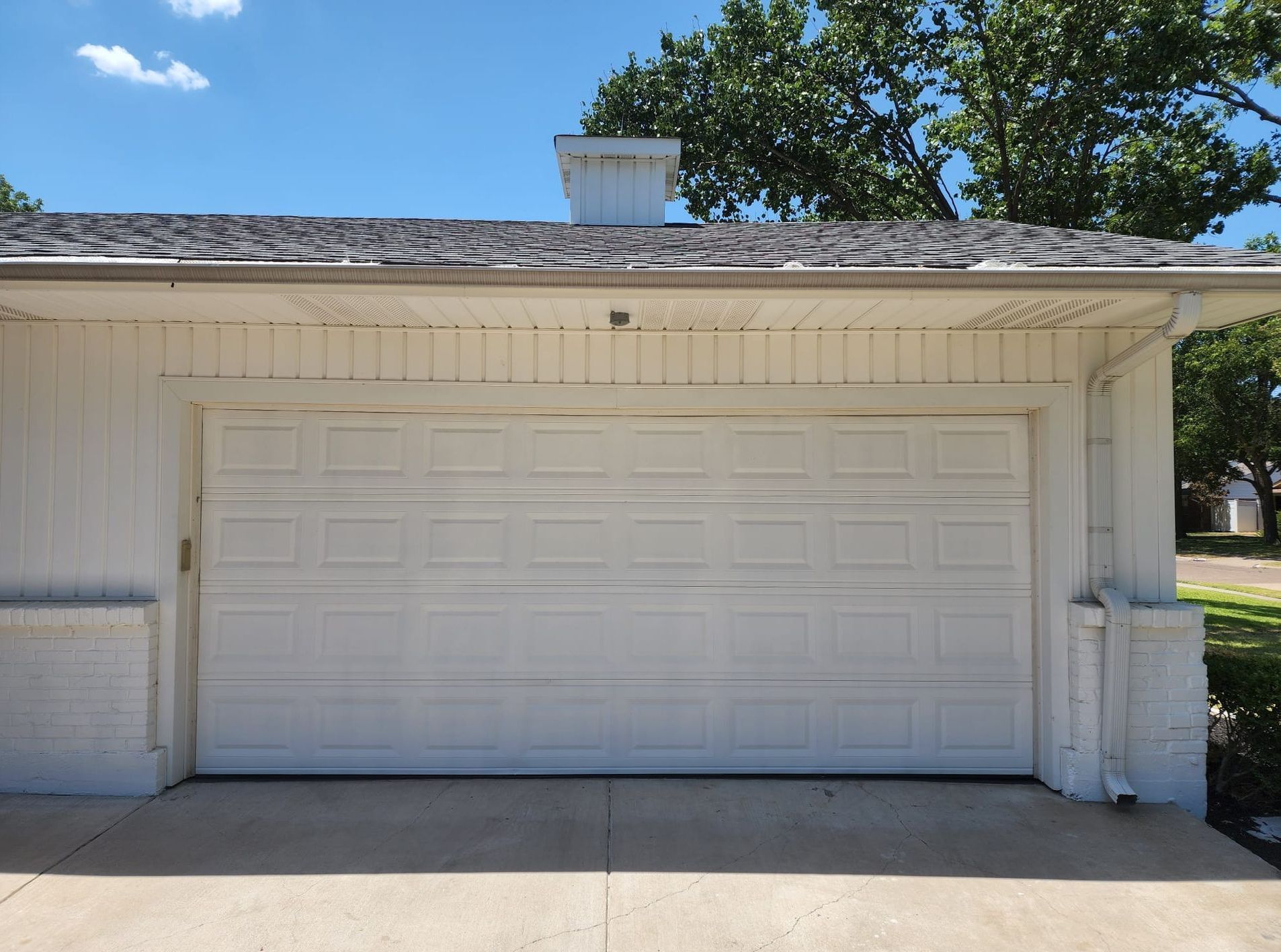 White garage door on a concrete driveway, under a white roof. Bright sunny day.