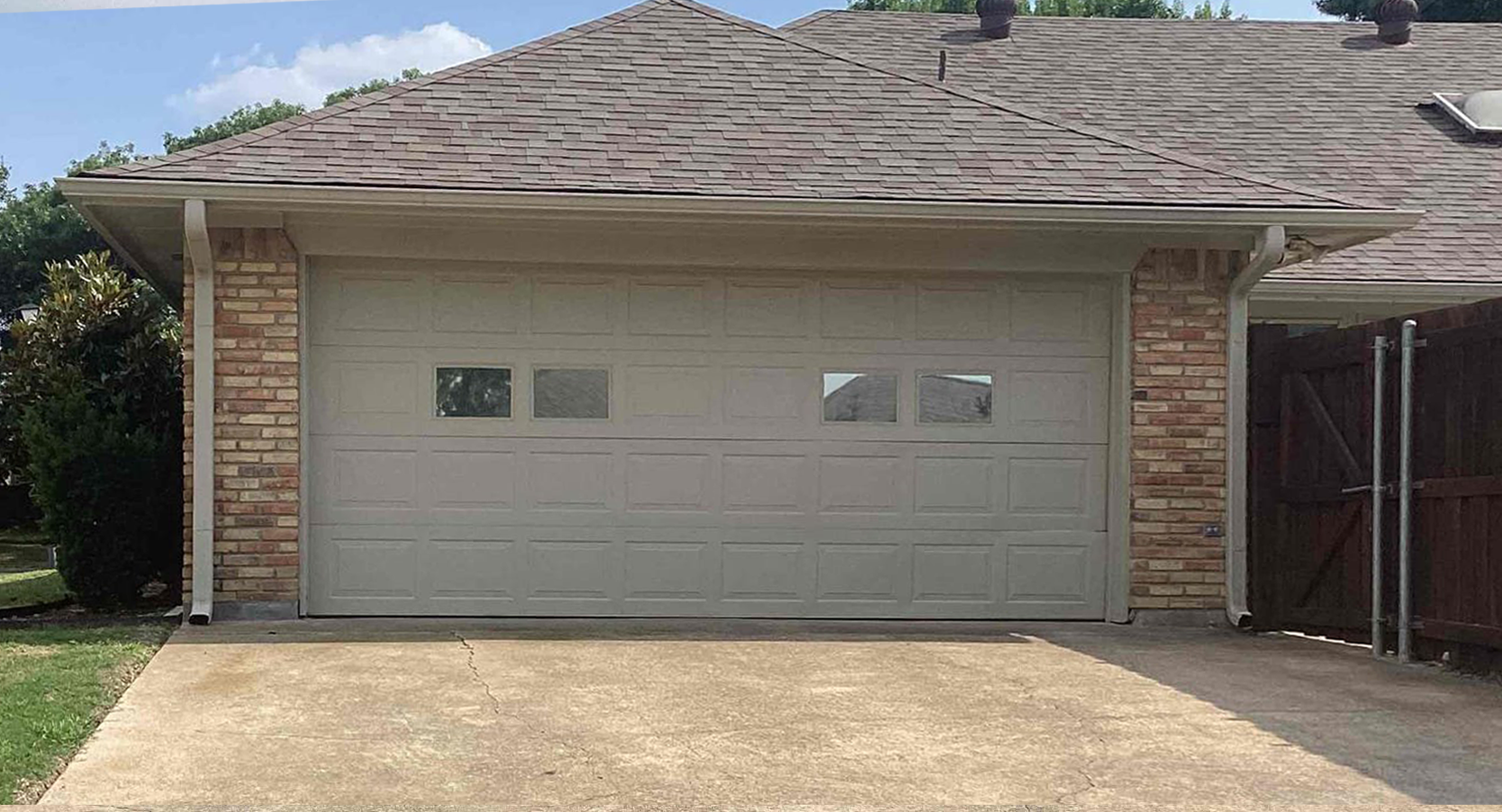 Garage with a light-colored door, stone accents, and a brown roof, with a driveway and green grass.
