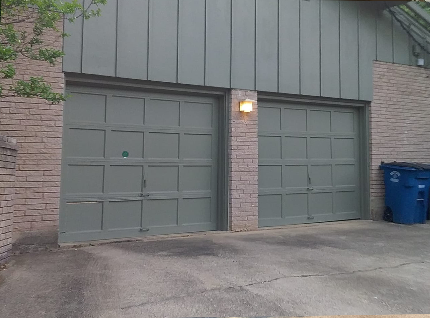 Two gray garage doors, brick exterior, blue trash cans.
