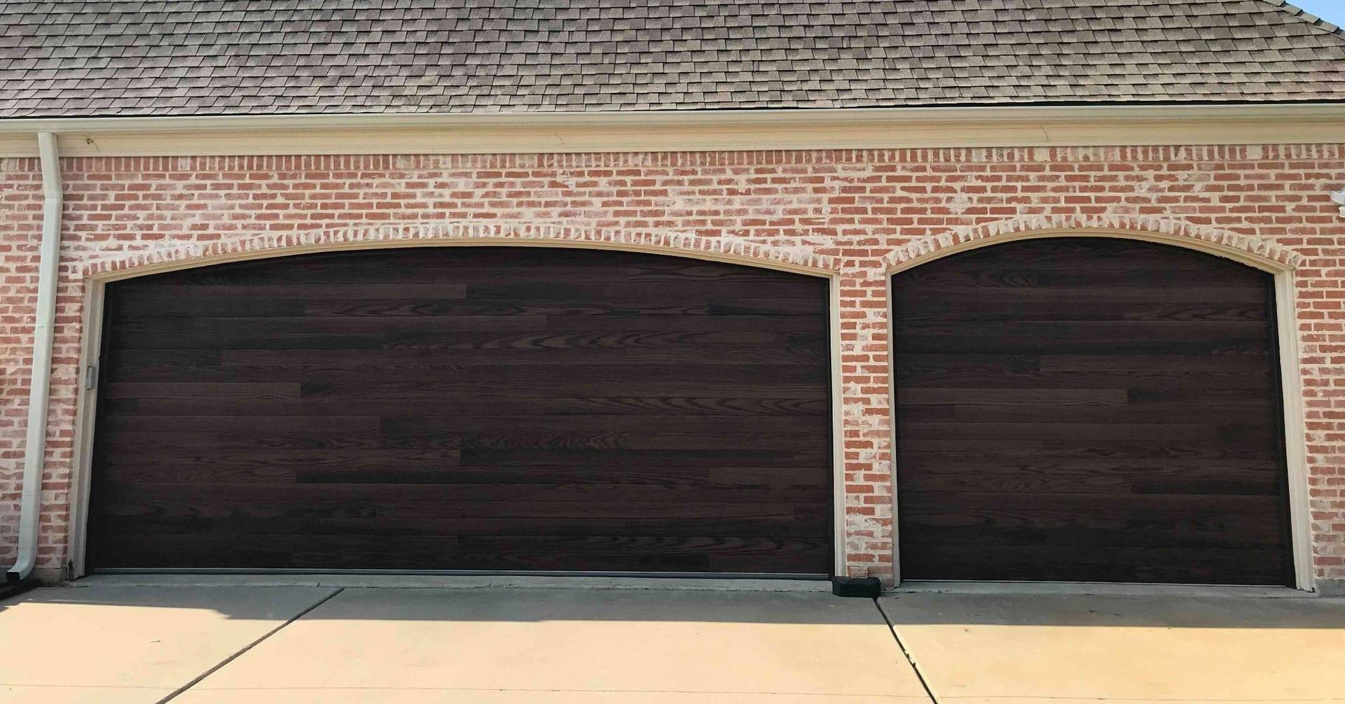 Two dark wood garage doors set into a brick archway on a residential home exterior.