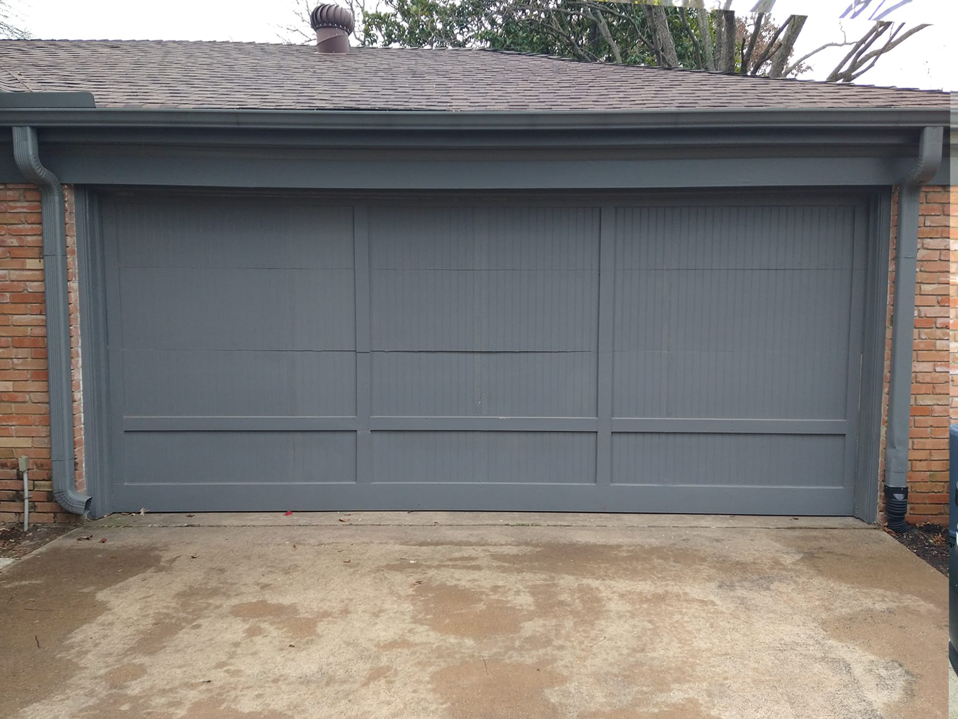 Gray garage door with brick trim, set on concrete driveway.