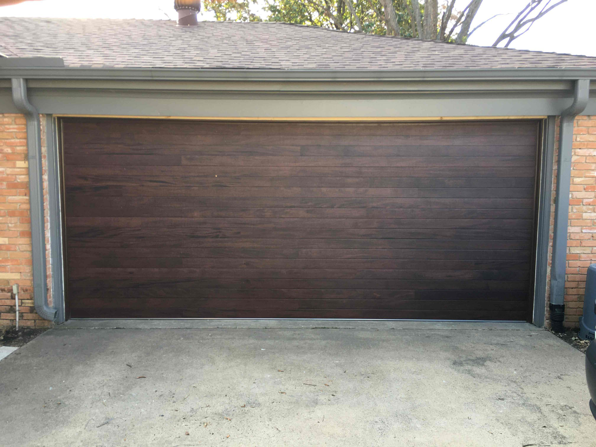 Dark brown garage door with a concrete driveway, set in a brick and grey-trimmed garage.