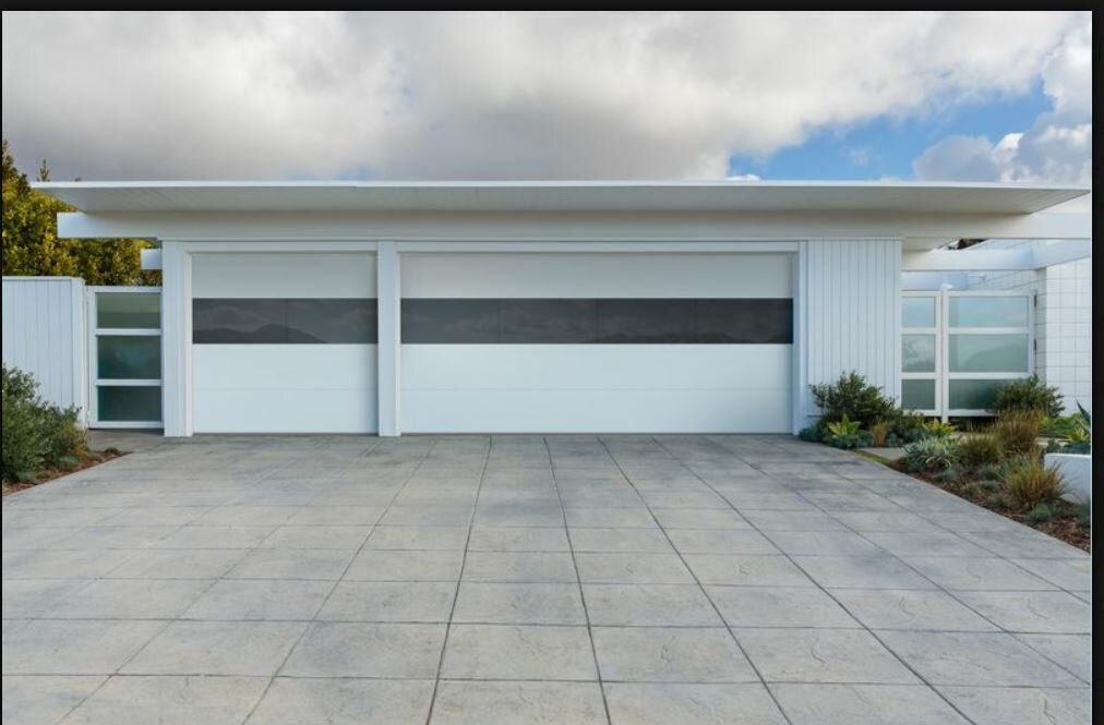 Modern house exterior featuring a wide garage with white doors and a horizontal dark gray stripe, with a paved driveway.