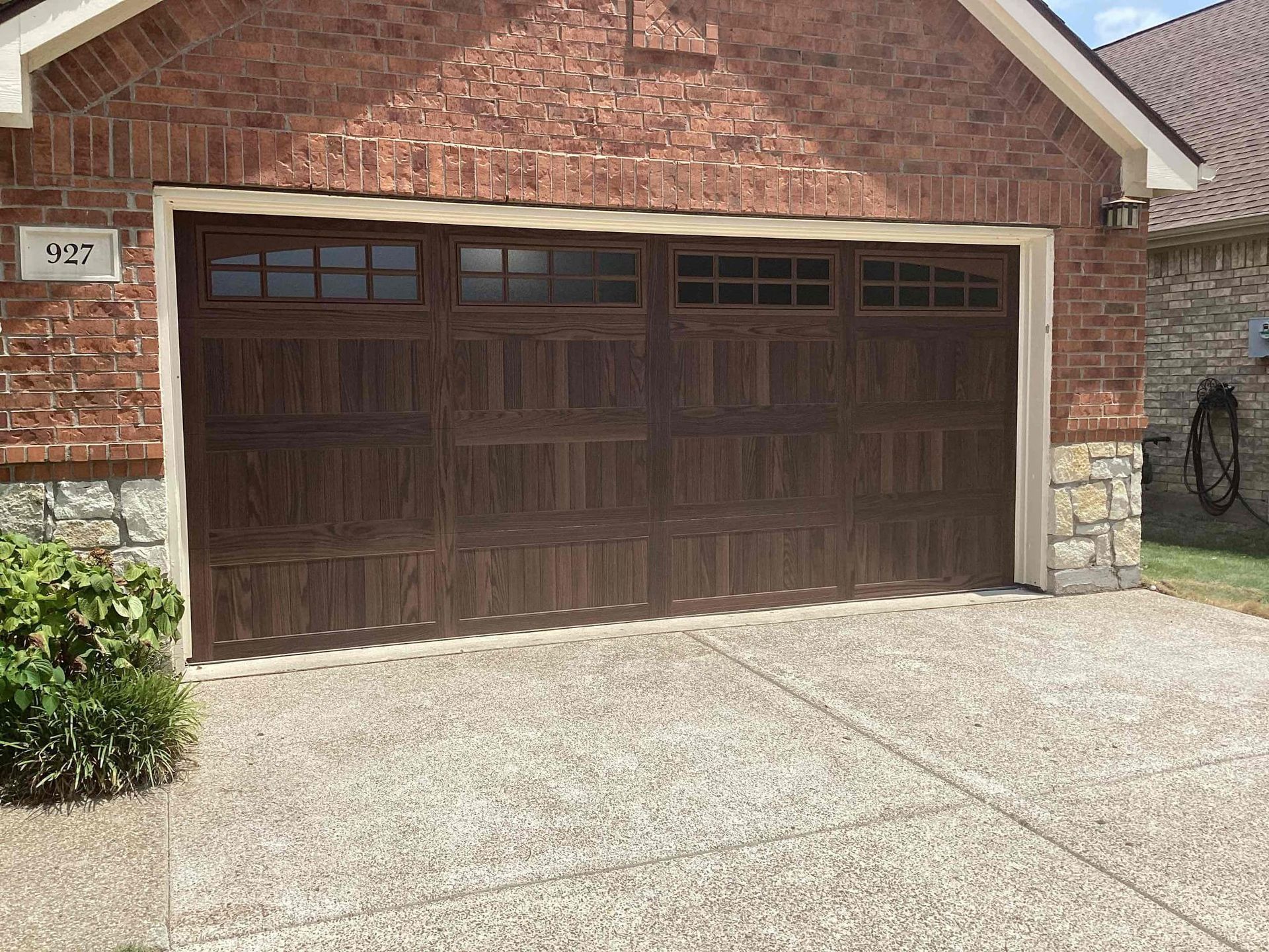 A dark brown, multi-paneled garage door with windows across the top, set into a red brick house with stone accents.