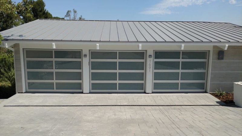 A modern three-car garage with white frames and frosted glass panels beneath a gray metal roof.