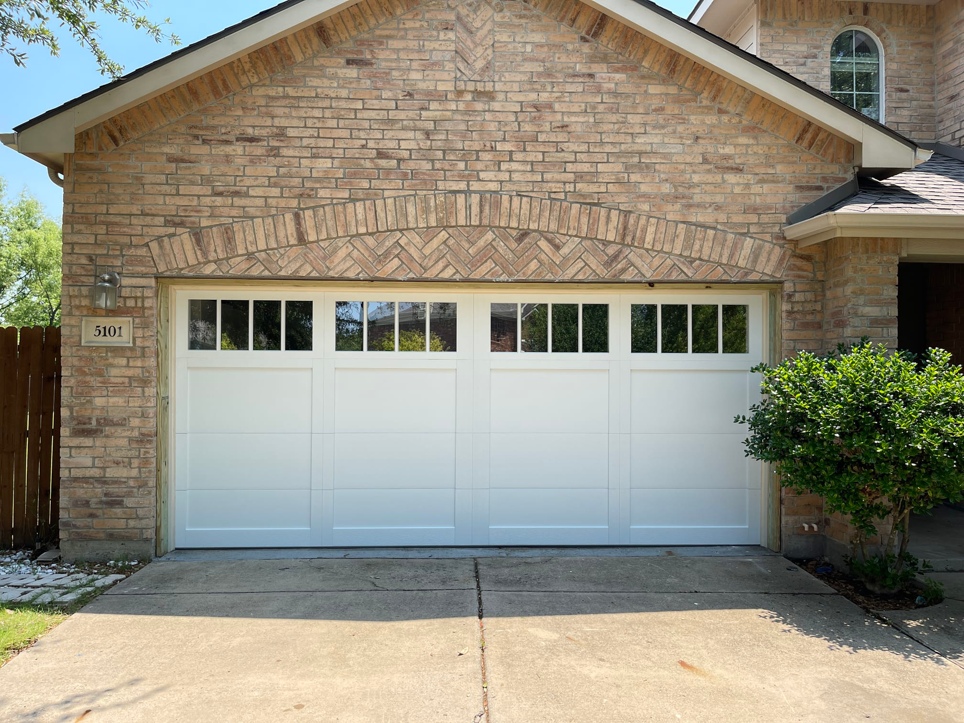 White garage door with window panels, in front of a brick facade.