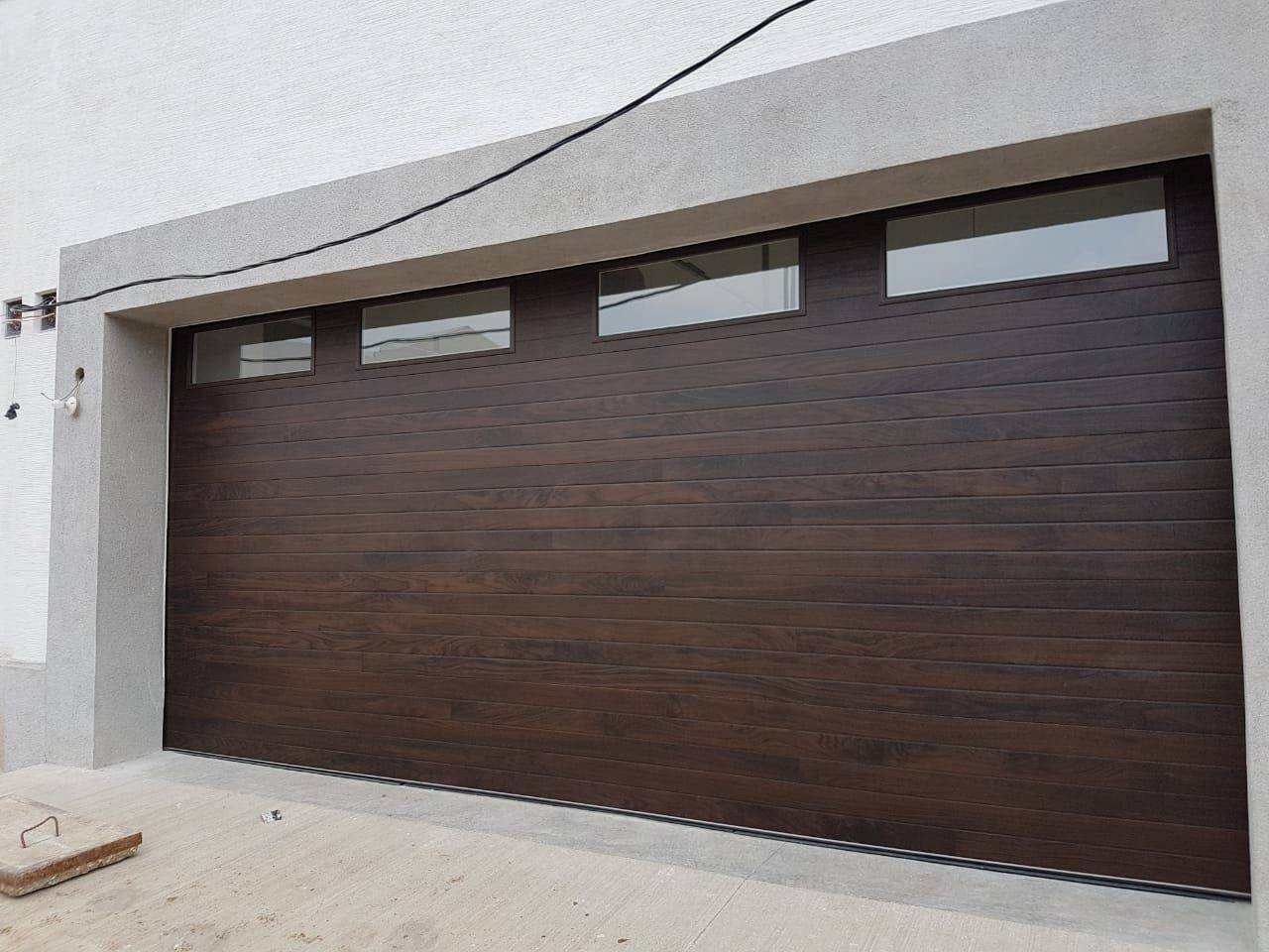 A dark wood-textured garage door with a row of four rectangular windows set in a concrete frame.