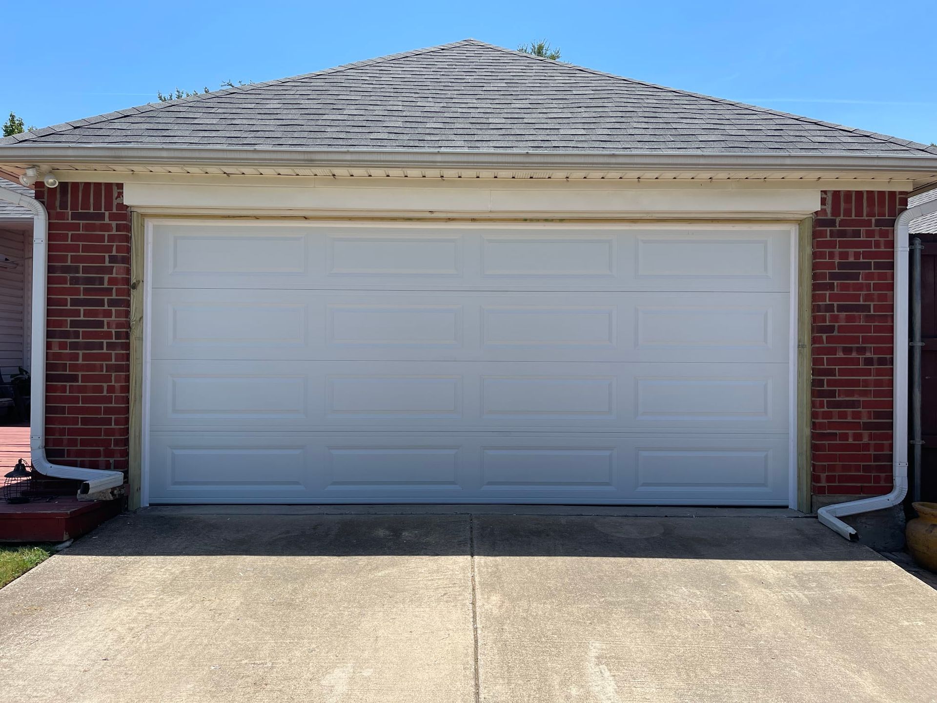 A white, rectangular garage door installed on a brick building with a gray, shingled hip roof.