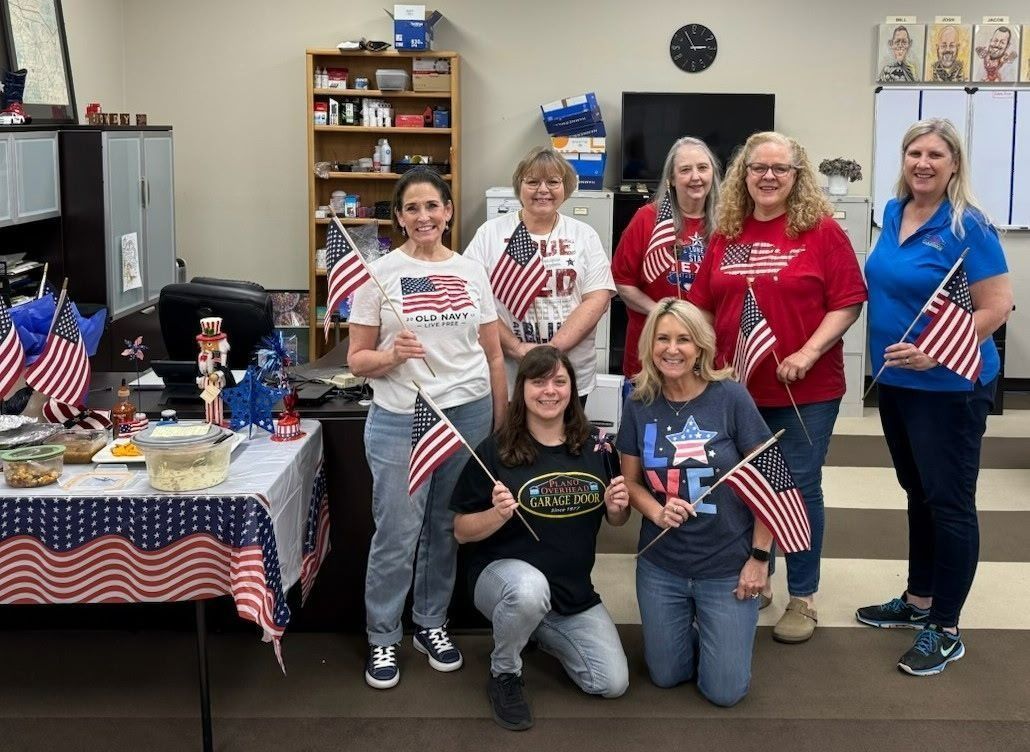 Group of people in a decorated room, holding American flags. Patriotic theme with red, white, and blue colors.