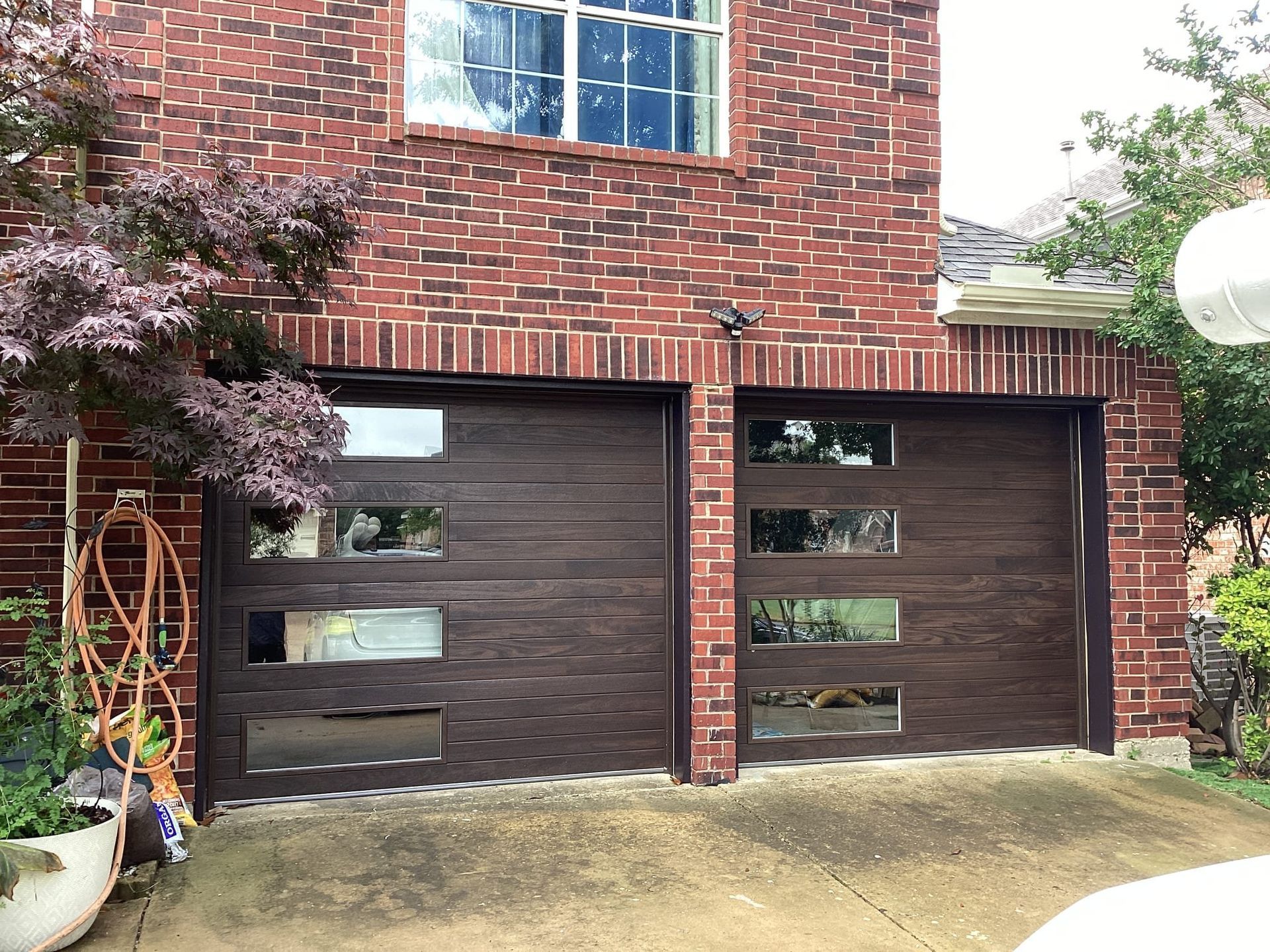Two brown garage doors with rectangular glass windows on a brick house.