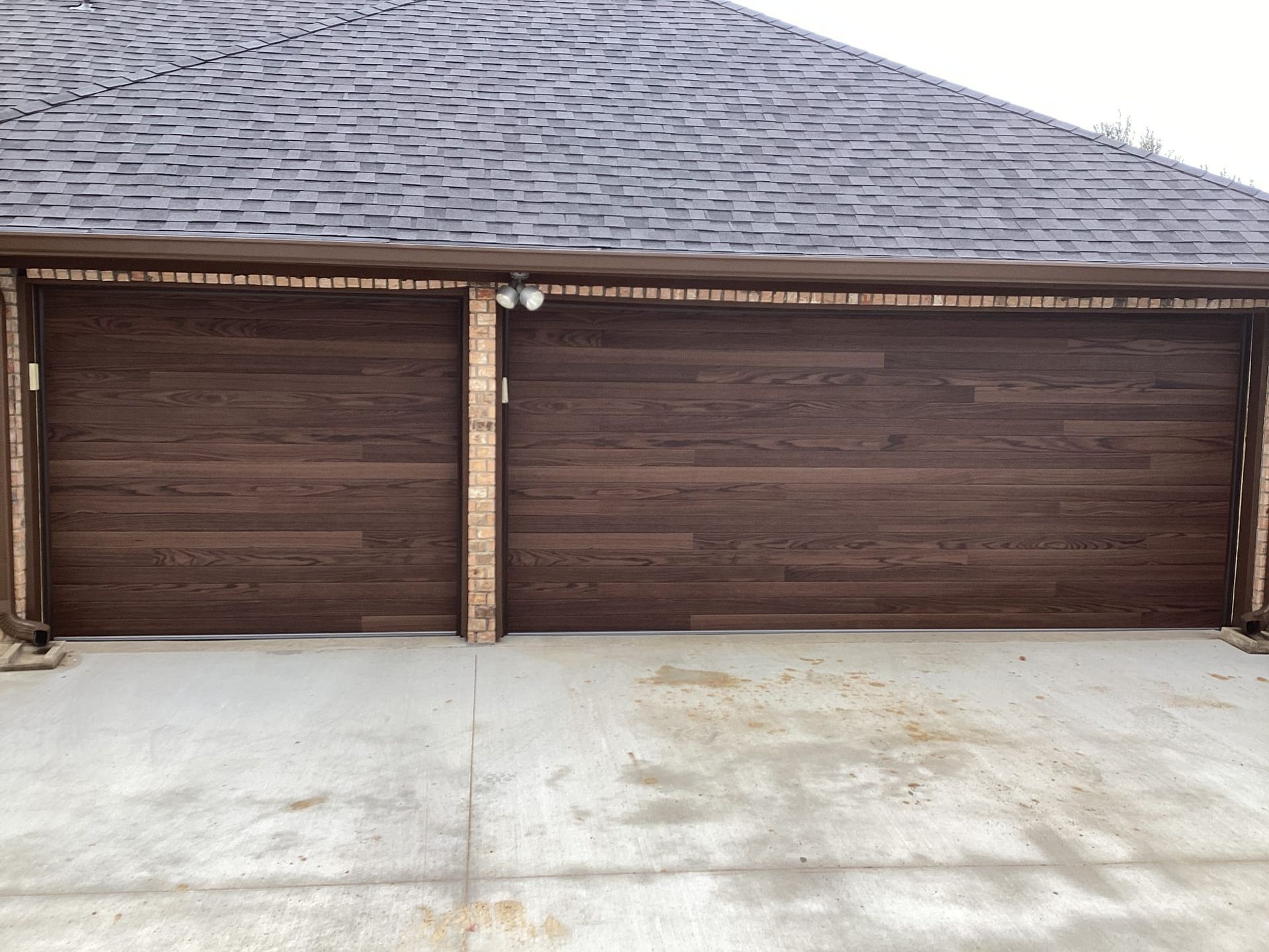 A two-car garage with horizontal, dark wood-finish garage doors and a brick pillar under a dark shingled roof.
