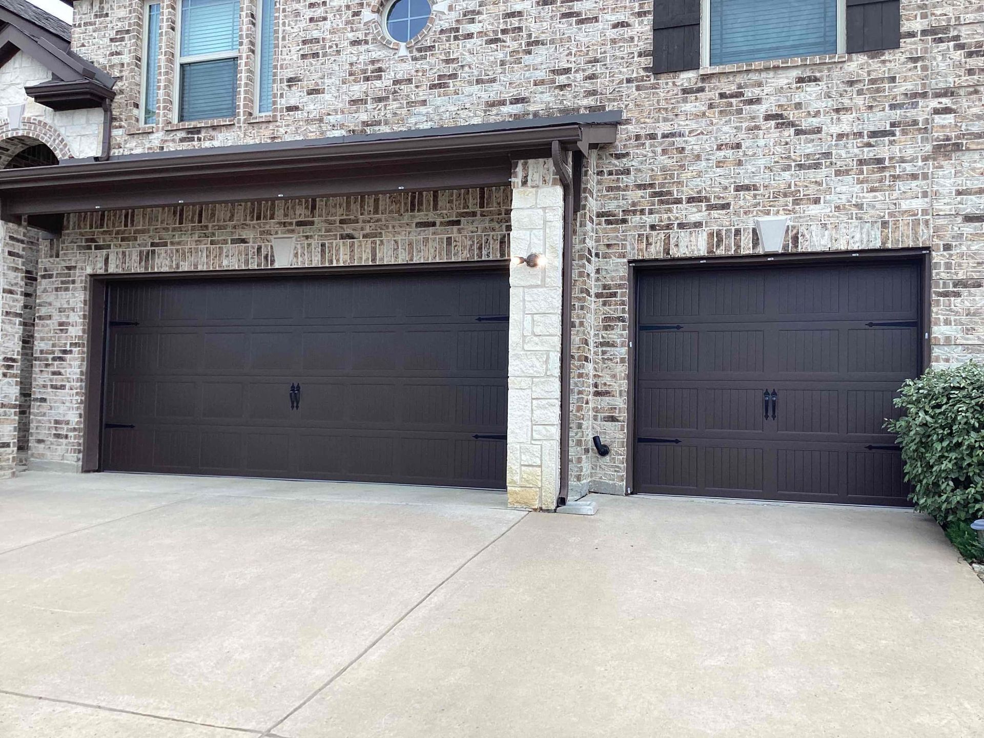 A two-car garage with dark brown paneled doors and a concrete driveway in front of a light-colored brick house.