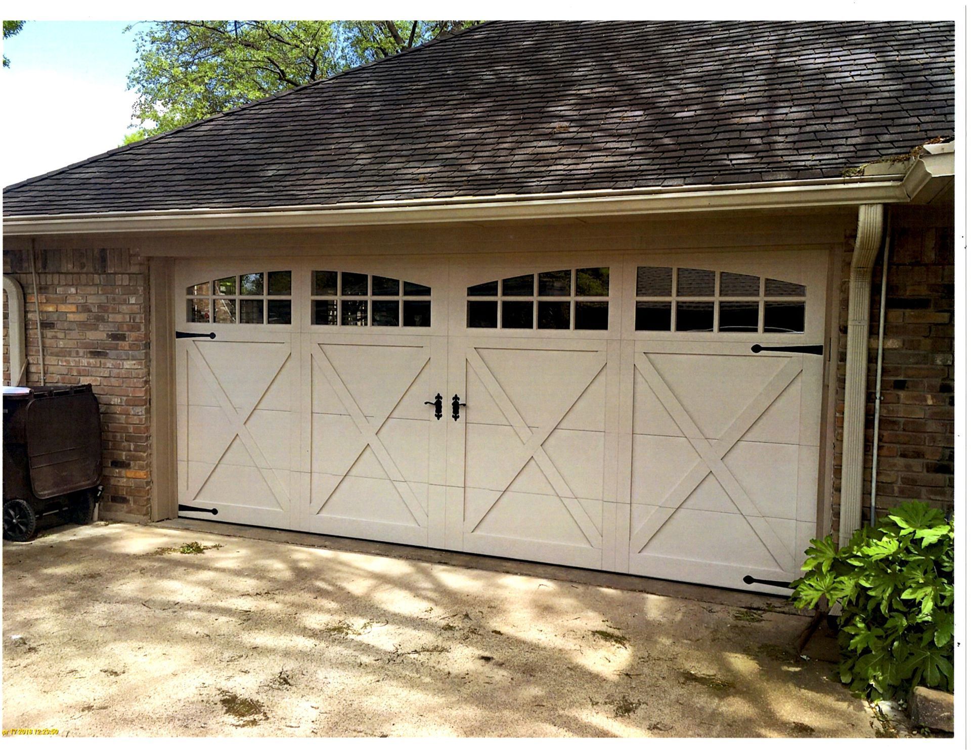 A white, wood-style carriage house garage door with four windows and an X-brace design, set in a brick exterior wall.