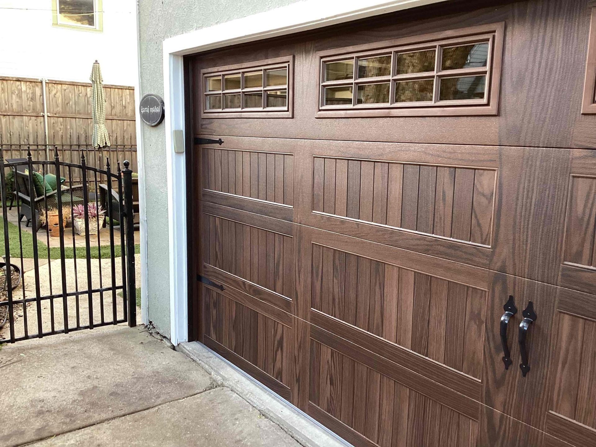 A dark wood-toned garage door with rectangular window panels and black decorative handles, viewed from a side angle.