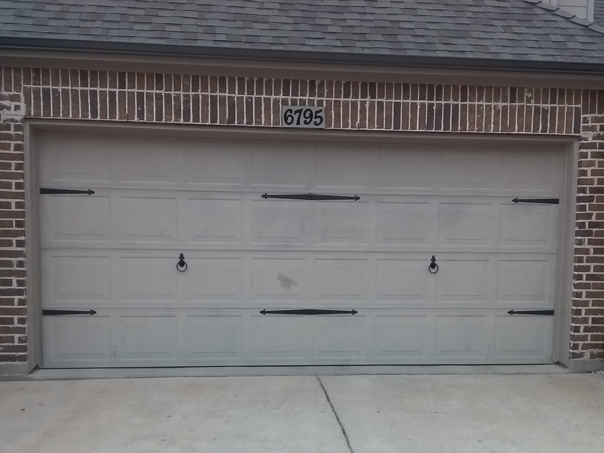 Garage door with decorative hardware, set in a brick facade, driveway in front.