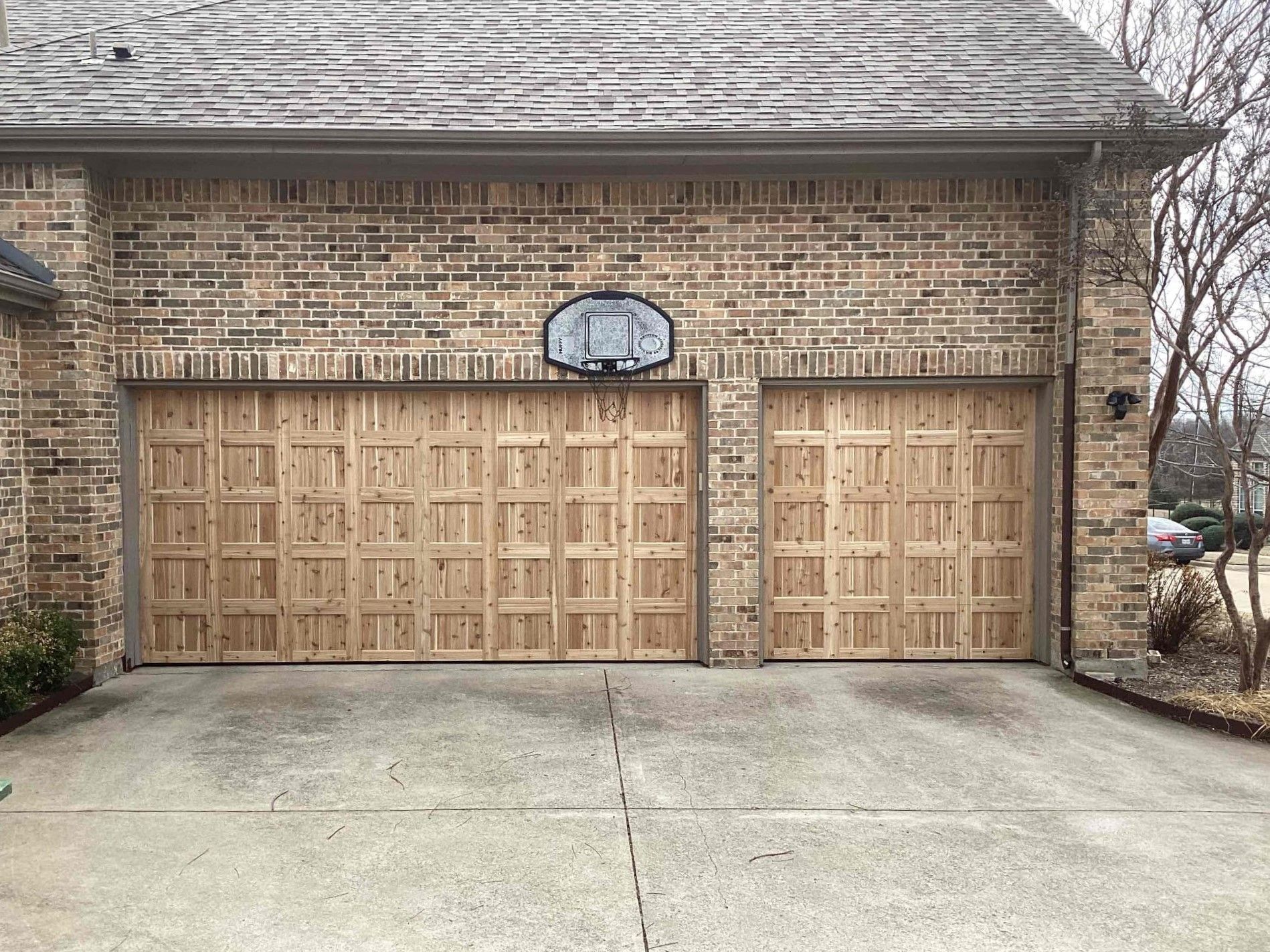 A two-car garage with light-colored wooden doors and a basketball hoop mounted on the brick exterior above.