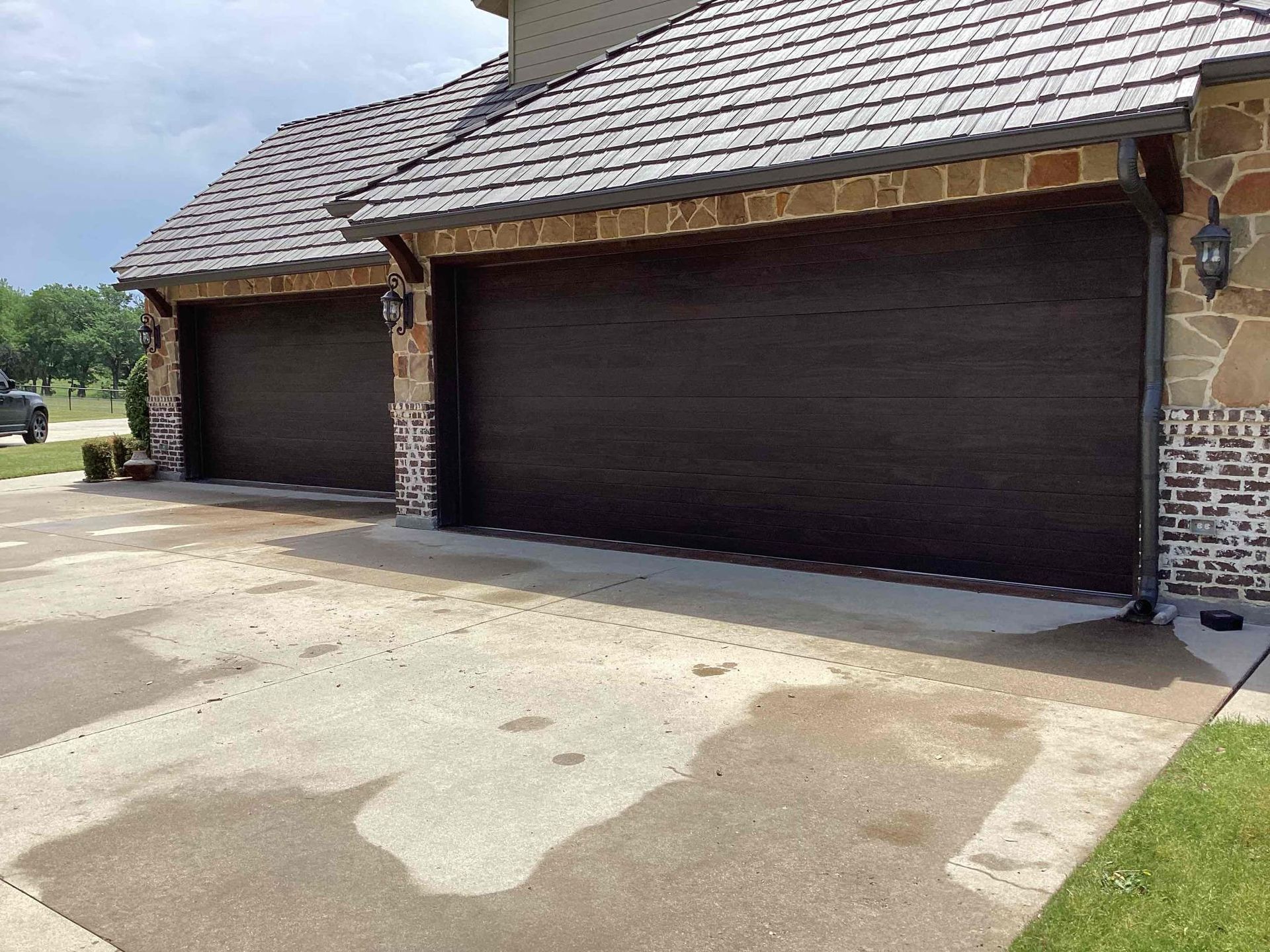 A suburban home exterior featuring two dark brown garage doors and stone accents on the driveway side.