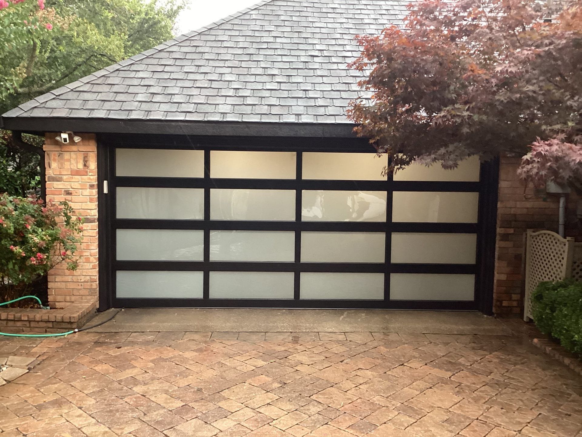 Modern garage door with a black frame and frosted glass panels, set in a brick exterior home.