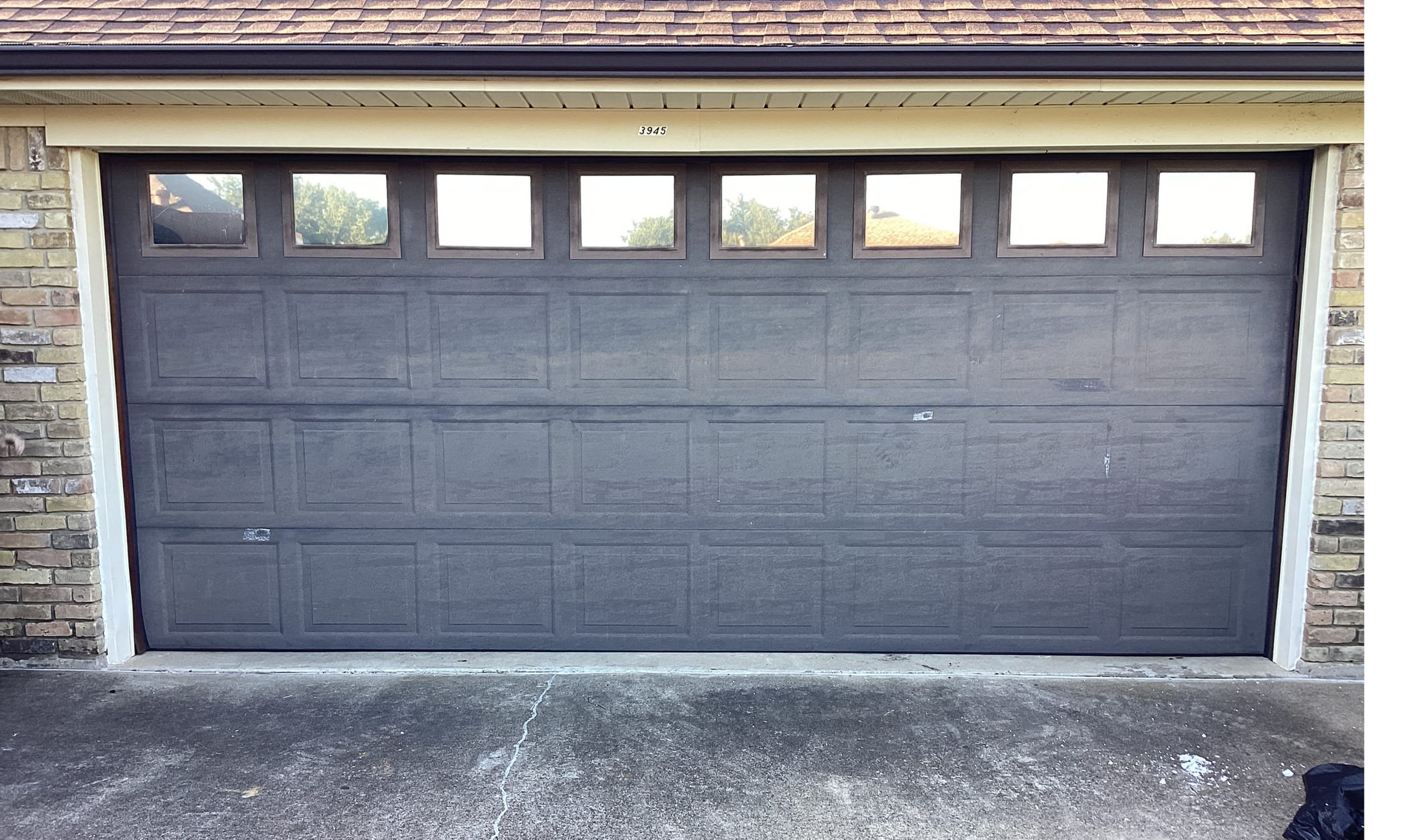 Gray garage door with window panels, in front of a brick building.