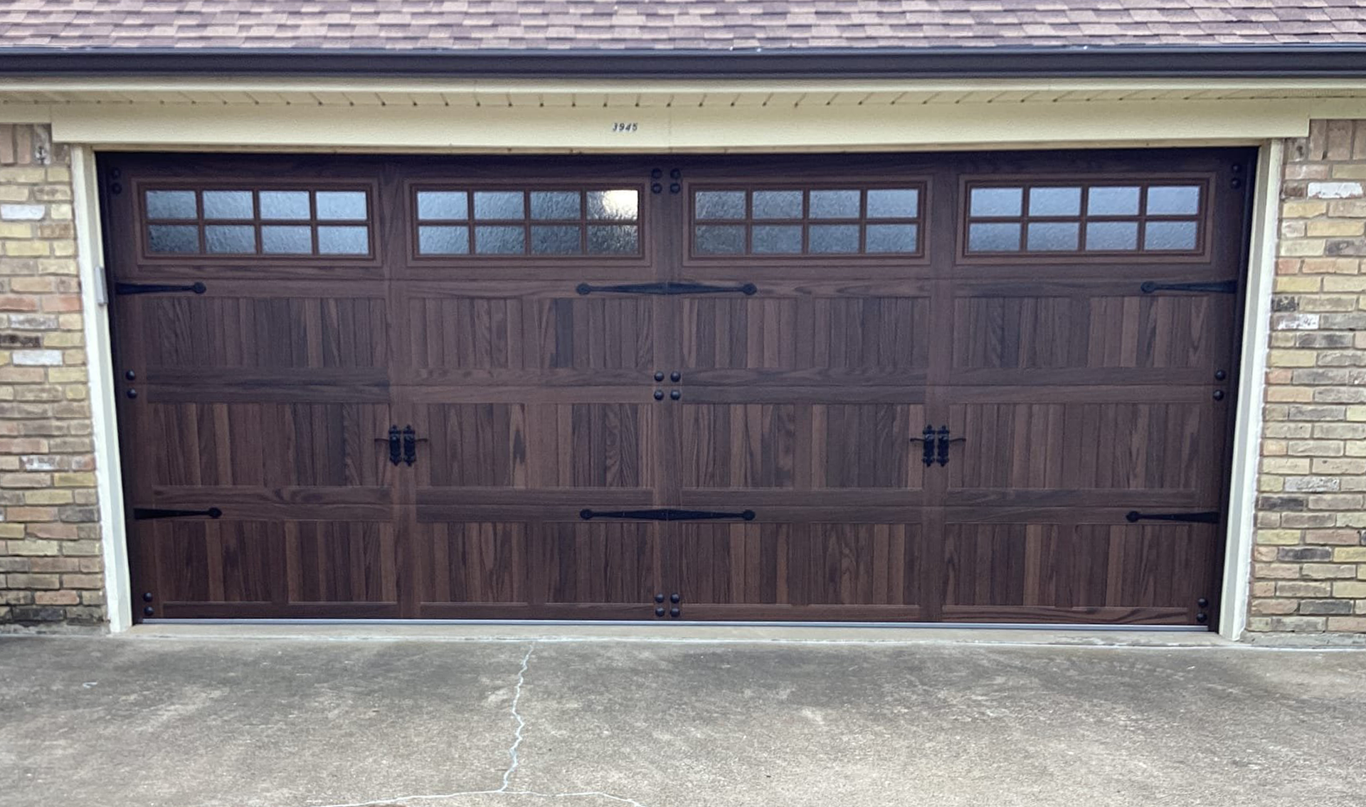 Brown garage door with decorative hardware and window panels. Brick building.