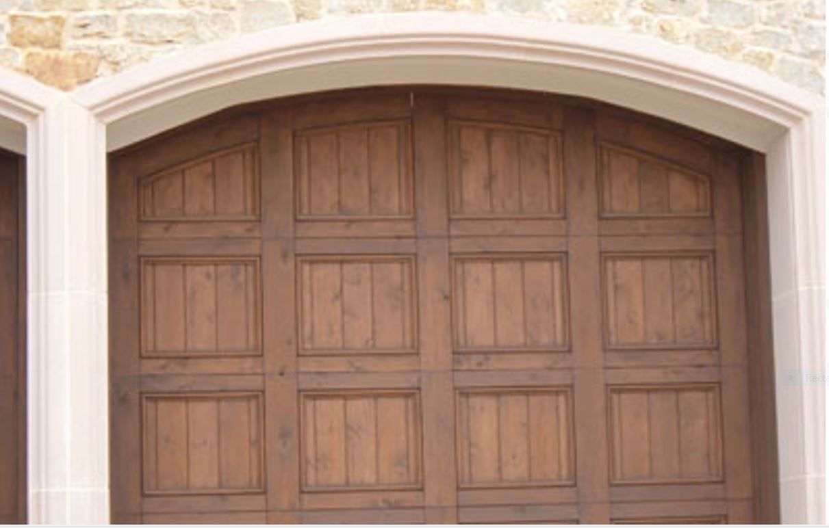 A close-up of a wooden garage door with a curved arch top and rectangular panels, set within a stone-facade frame.