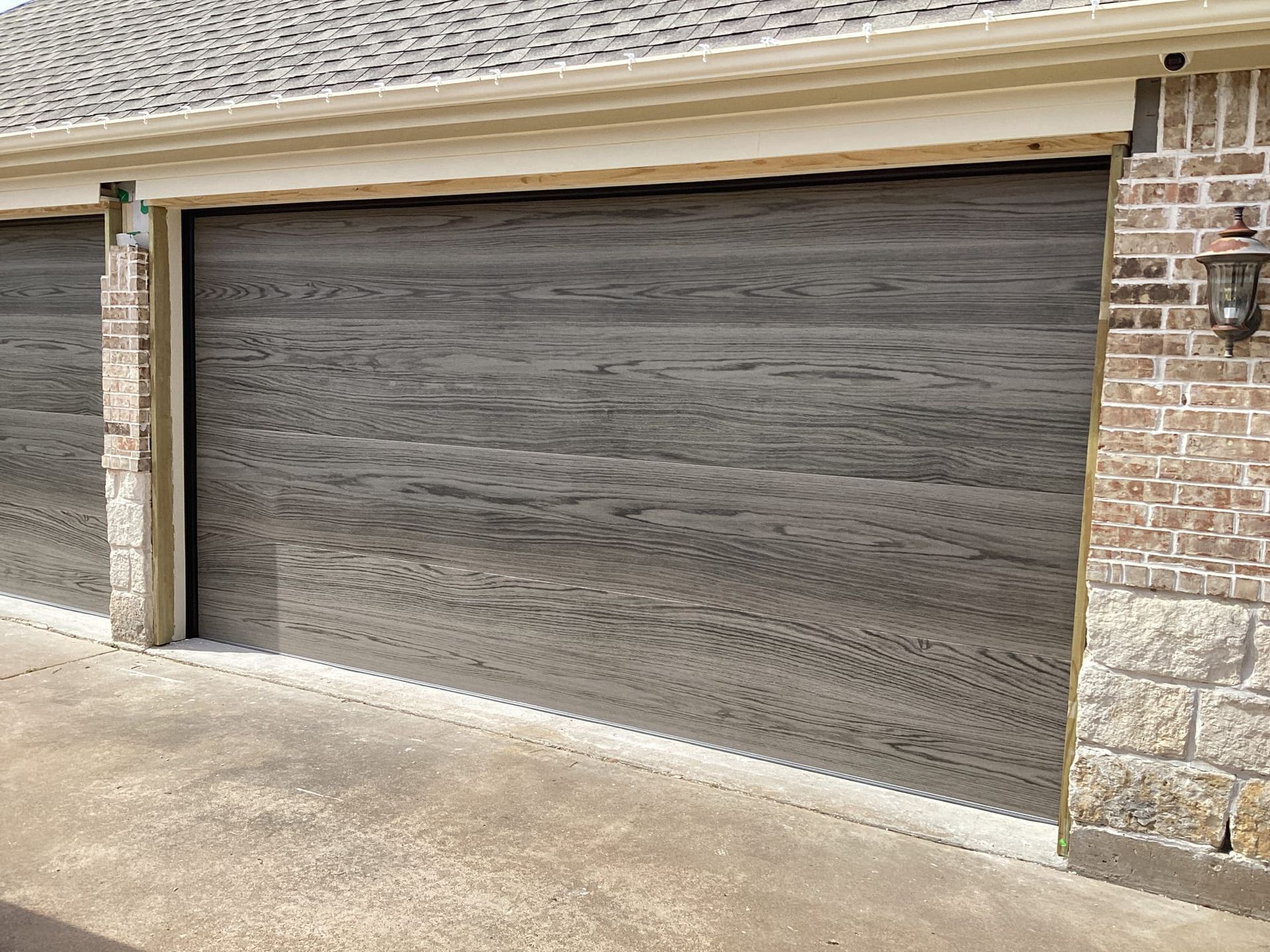 Dark-stained wooden garage doors with a horizontal grain, set into a brick and stone exterior wall.