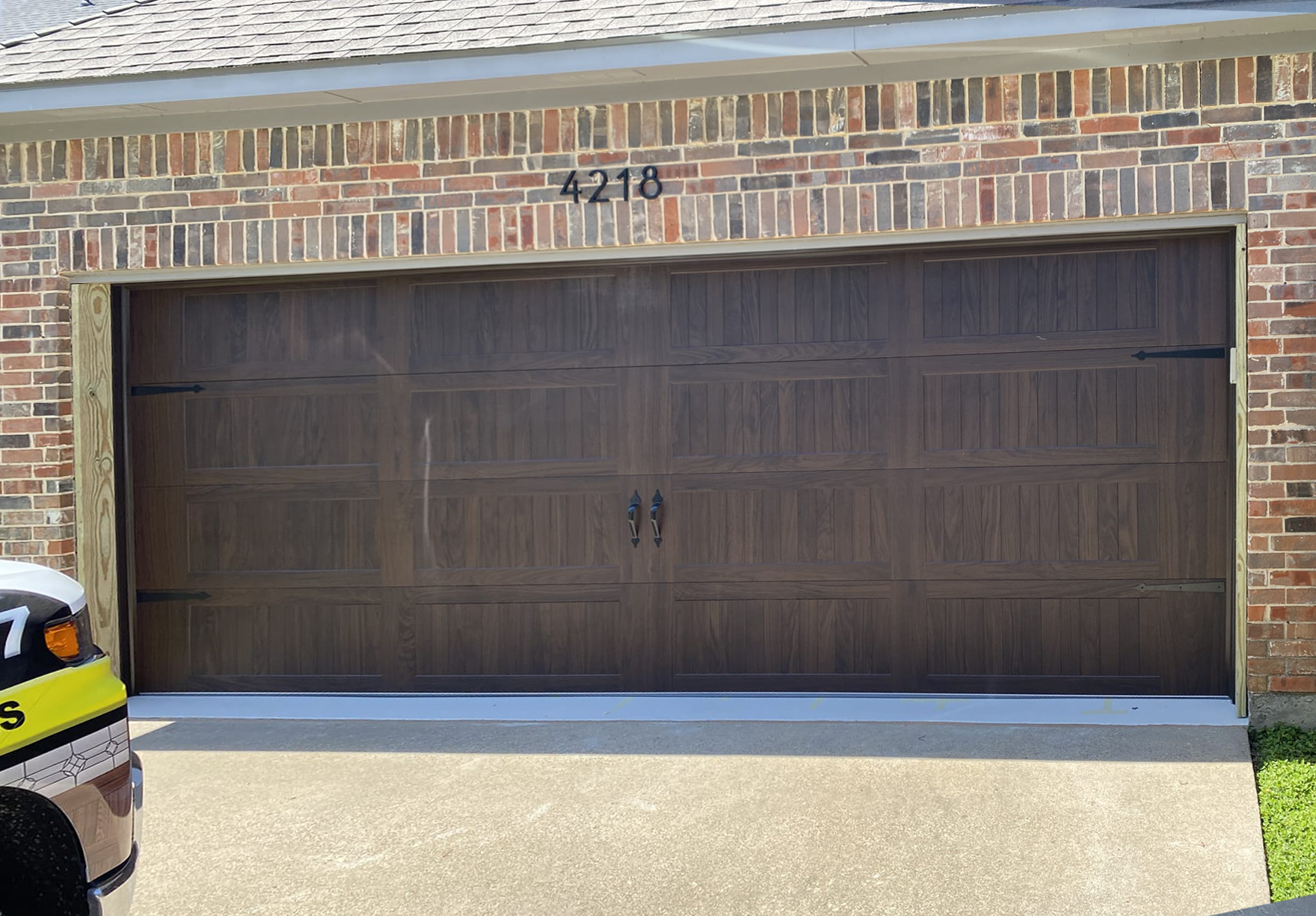 Brown garage door with black hardware, brick facade, and address number 