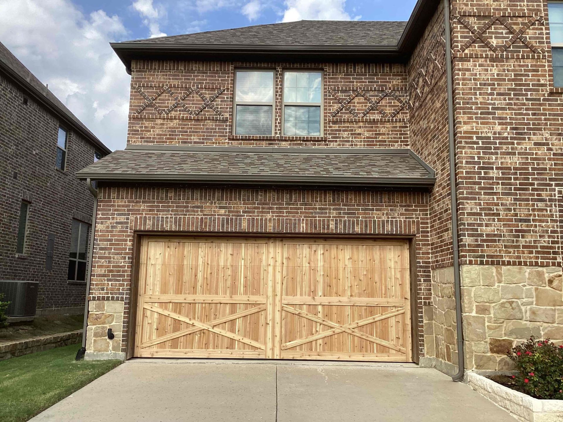 Two-story brown brick house with decorative masonry and a light wood garage door featuring an X-brace design.